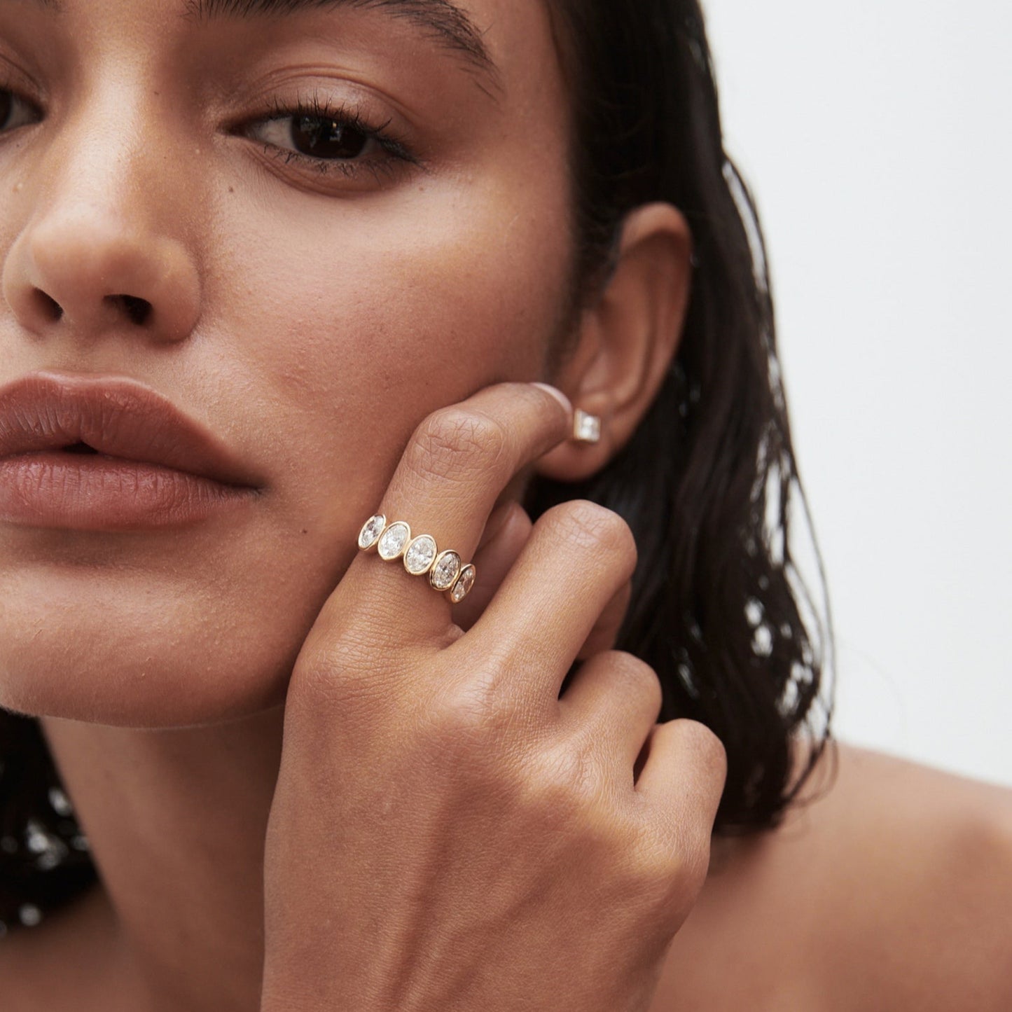 Close-up of a woman with wet hair showcasing a luxurious gold ring adorned with diamonds on her finger, conveying elegance and sophistication.