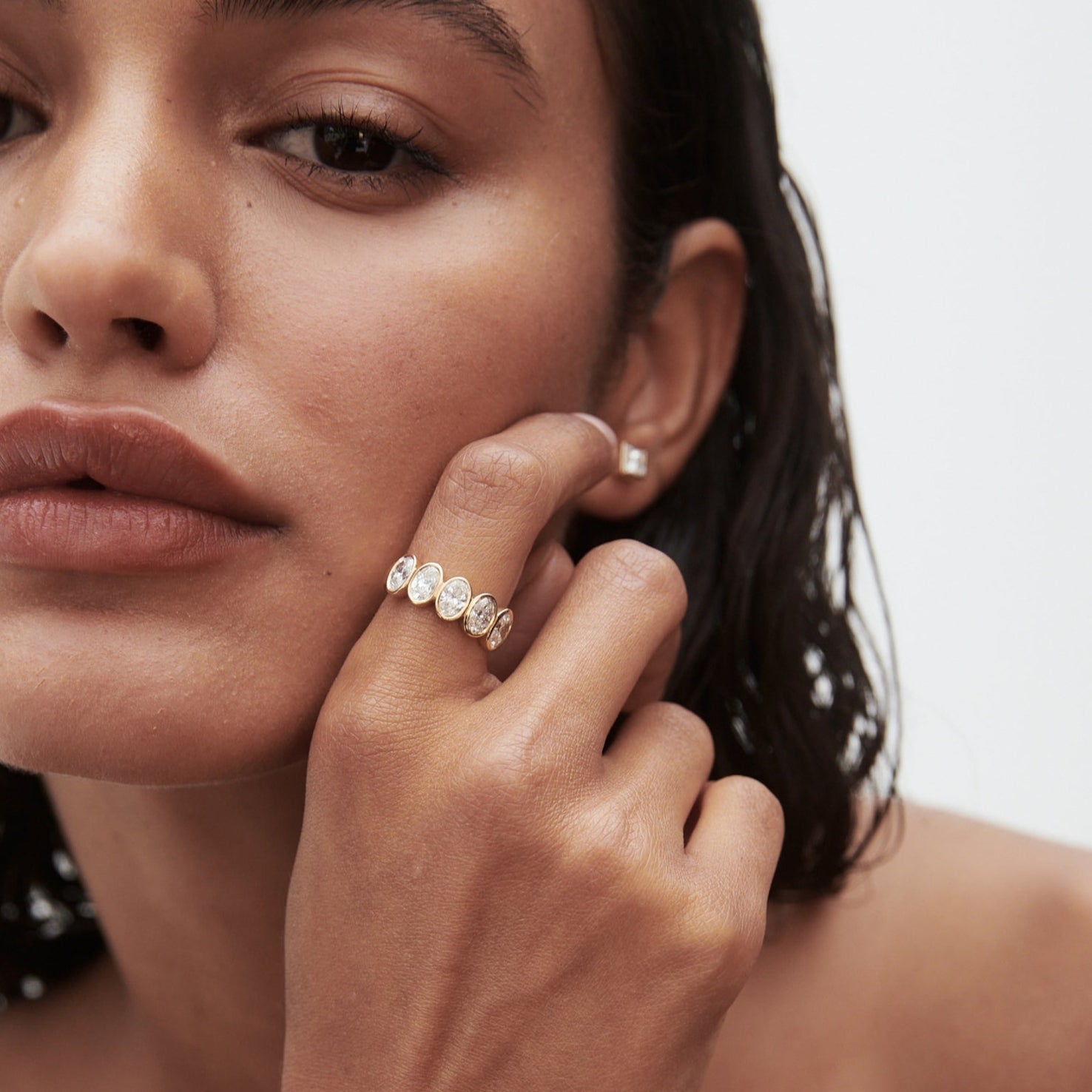 Close-up of a woman with wet hair showcasing a luxurious gold ring adorned with diamonds on her finger, conveying elegance and sophistication.