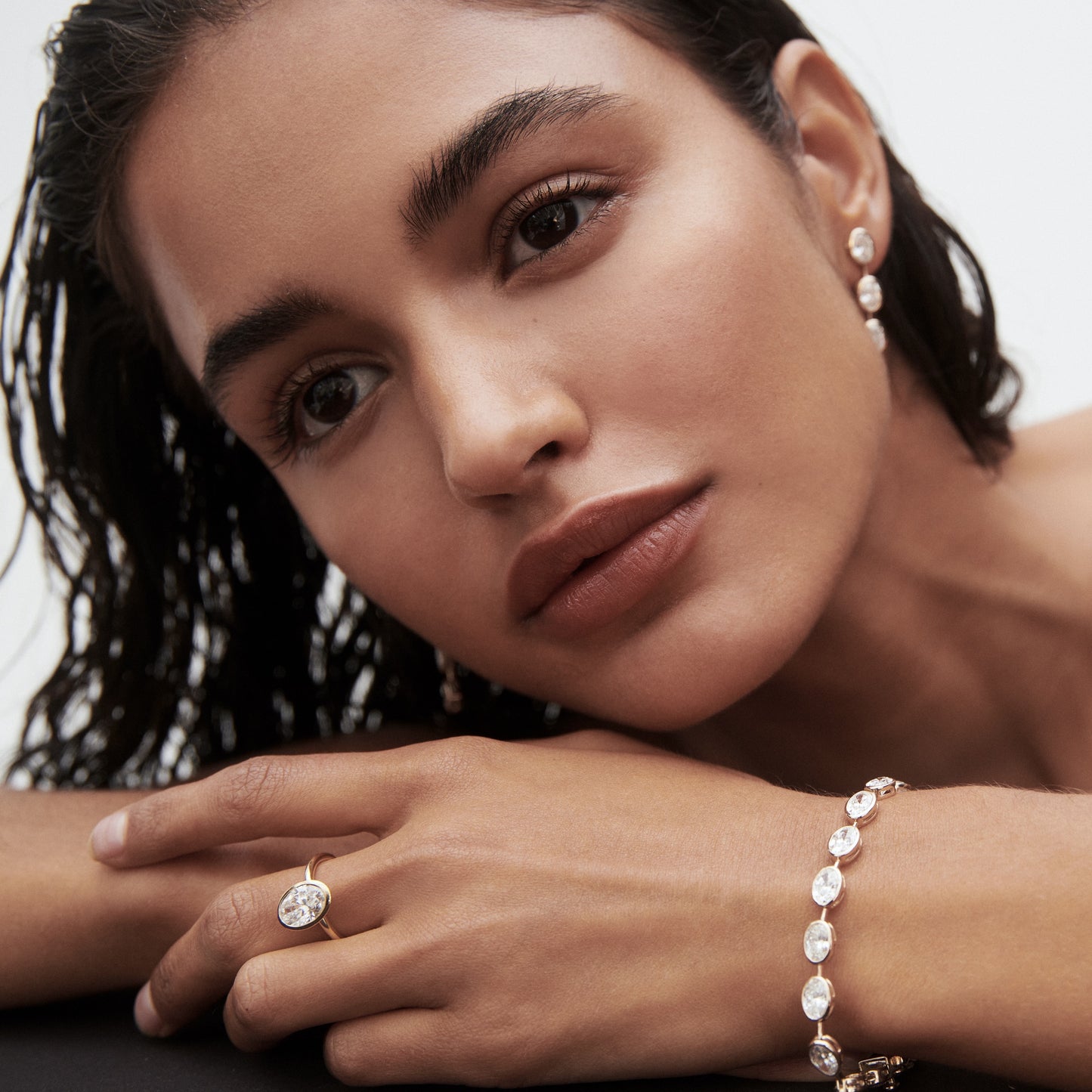 Woman wearing elegant diamond earrings, bracelet, and ring, with wet hair and neutral makeup, gazes softly, showcasing luxury jewellery.