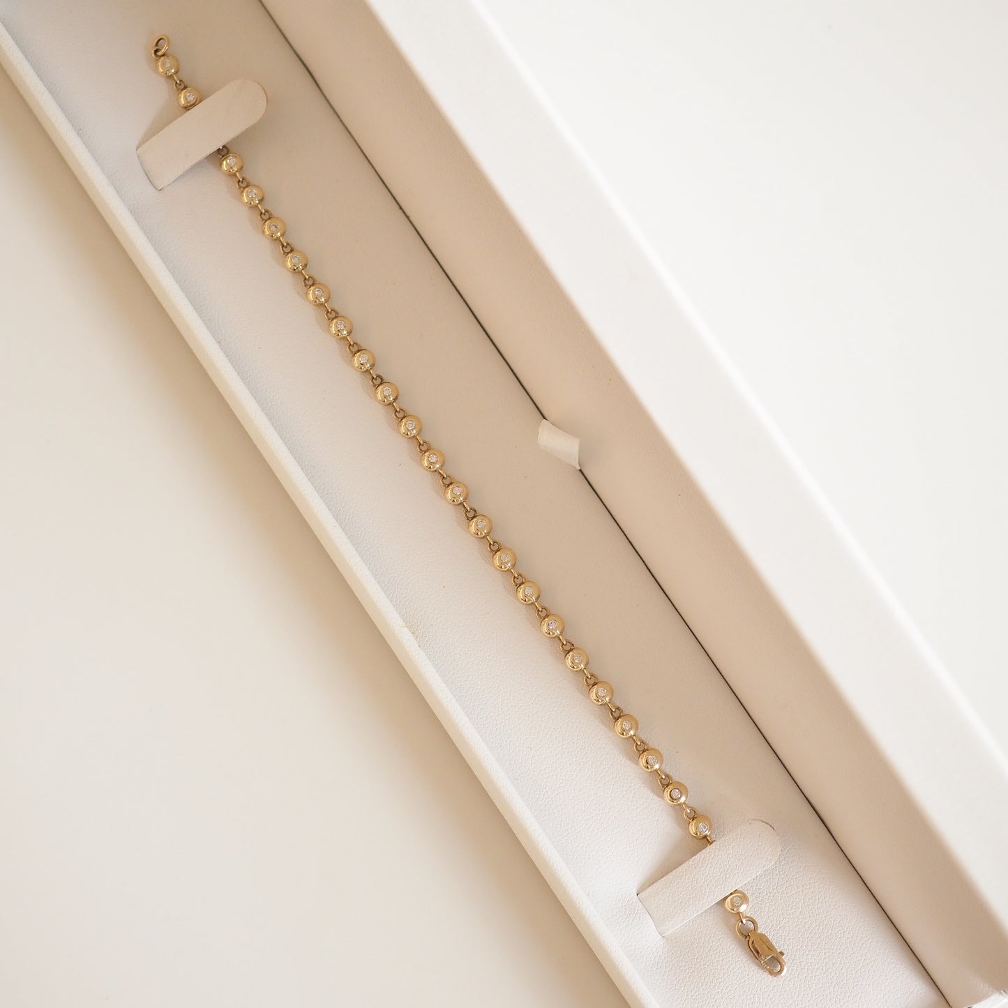 Gold bead bracelet in an elegant cream jewellery box, displayed diagonally. Ideal for luxury jewellery enthusiasts.