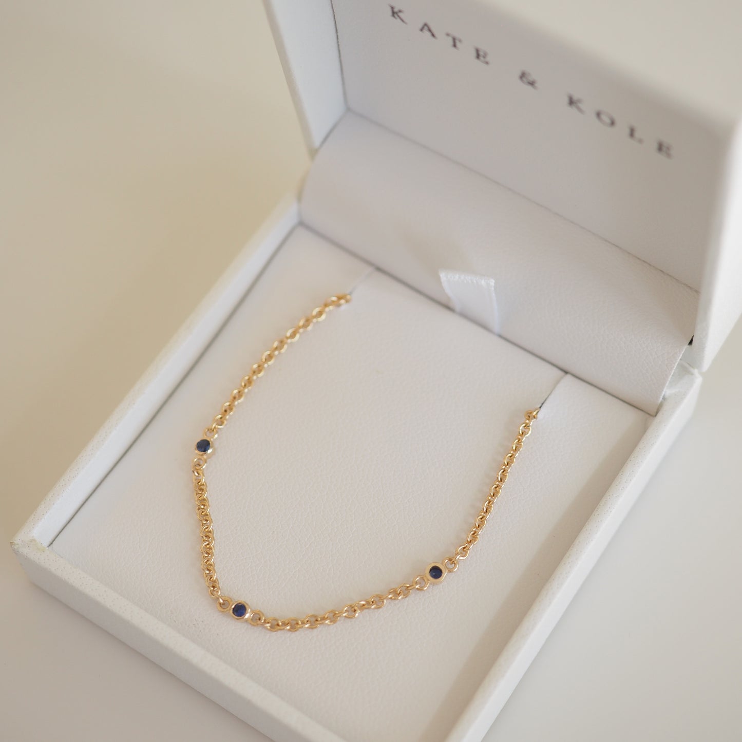 Gold bracelet with blue gemstones in a white Kate & Kole jewellery box. Elegant luxury accessory, perfect for sophisticated style.