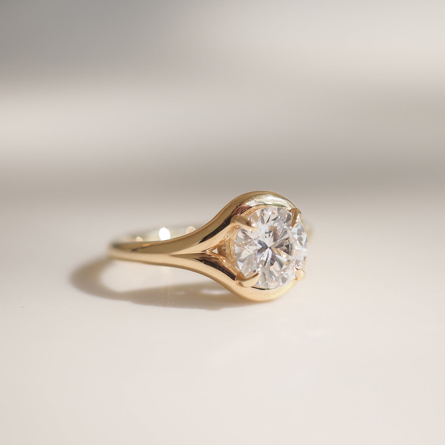 A large round diamond in a gold bezel setting ring, displayed on a soft, neutral background, showcasing luxury jewellery elegance.