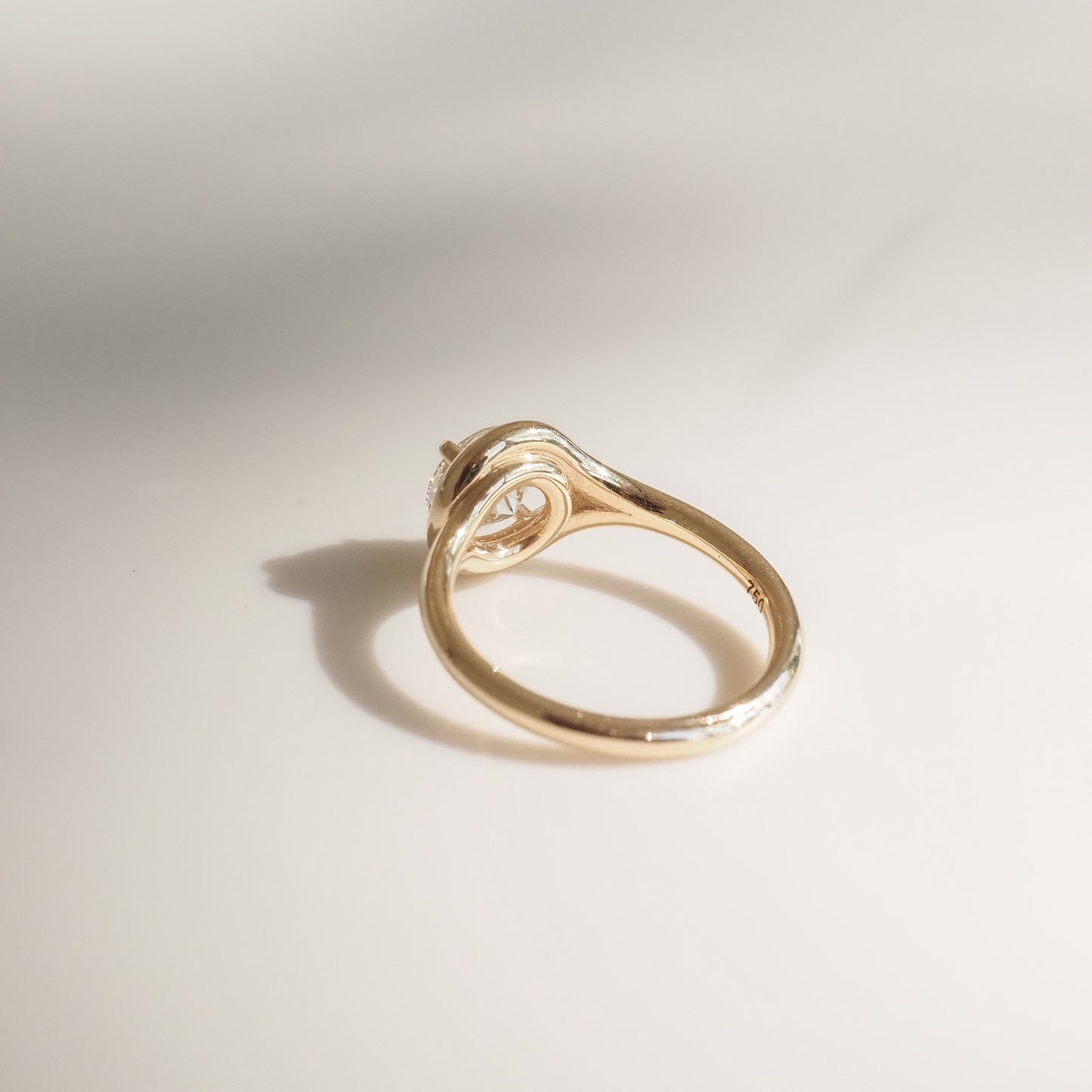 Elegant gold ring with a unique, twisted band design, set with a solitaire diamond, casting a soft shadow on a smooth surface.