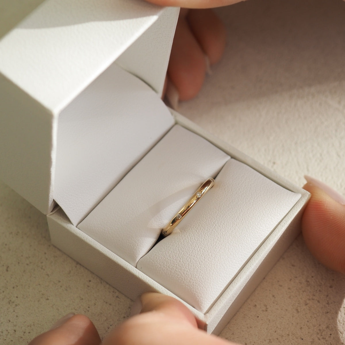 Luxury gold ring in an elegant white box, cradled by fingers. Perfect for engagements or high-end jewellery collections.