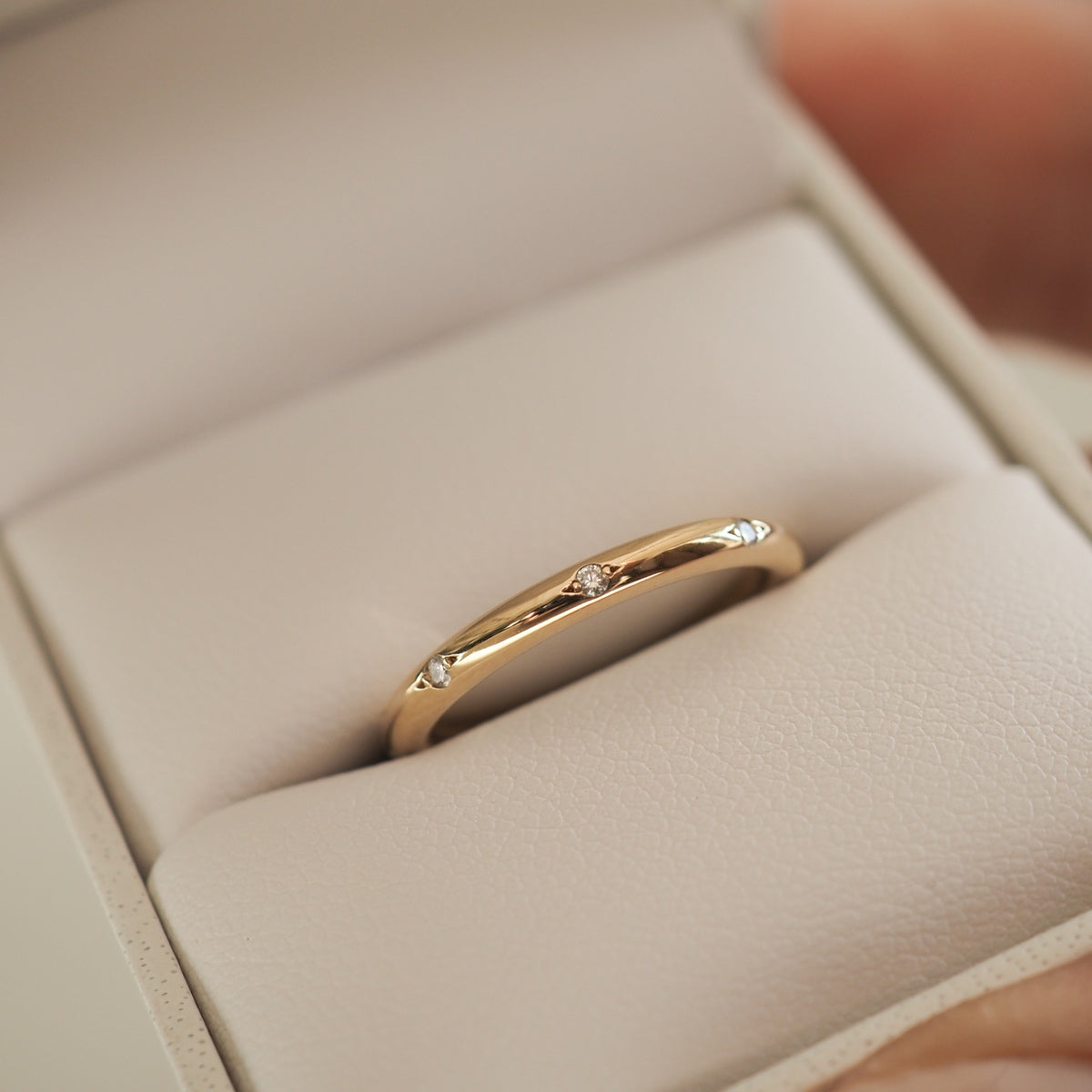 Gold ring with small round diamonds, elegantly set in a light jewellery box. Luxurious design, perfect for high-end fashion.