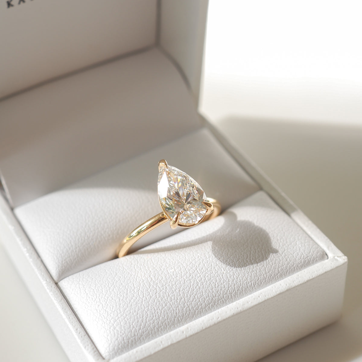 Pear-shaped diamond ring with a gold band displayed in an elegant white jewellery box, capturing luxury and sophistication.