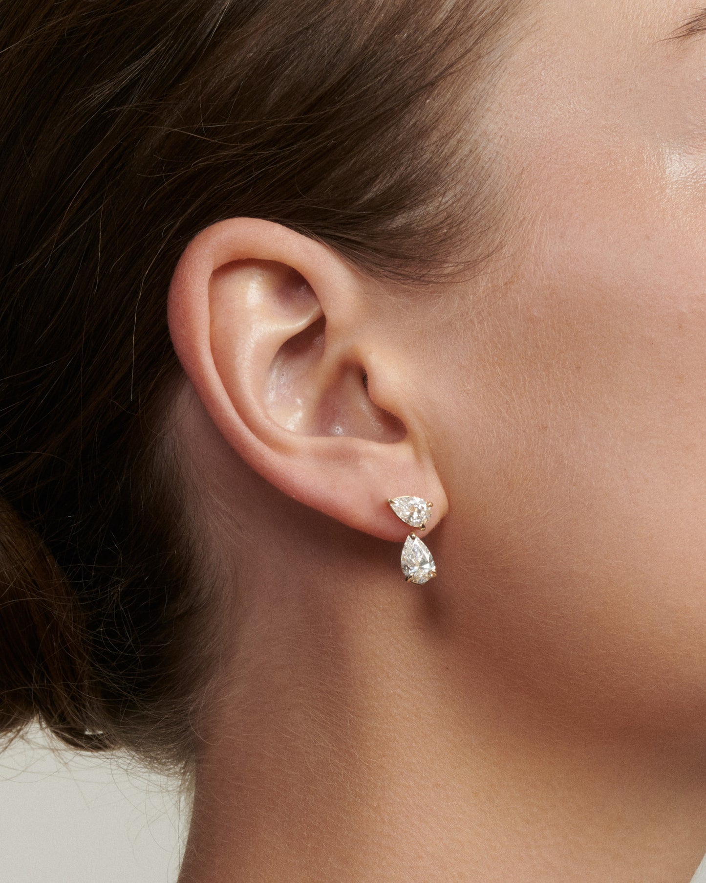 Close-up of a person wearing pear-shaped diamond earrings.
