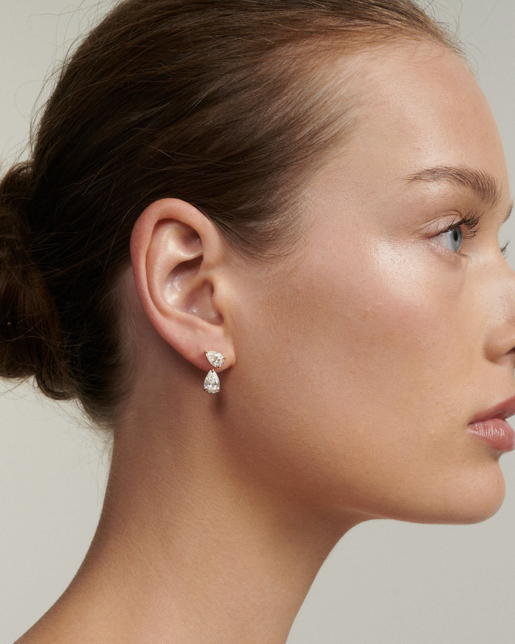 Close-up of a woman wearing pear-shaped earrings with a neutral background