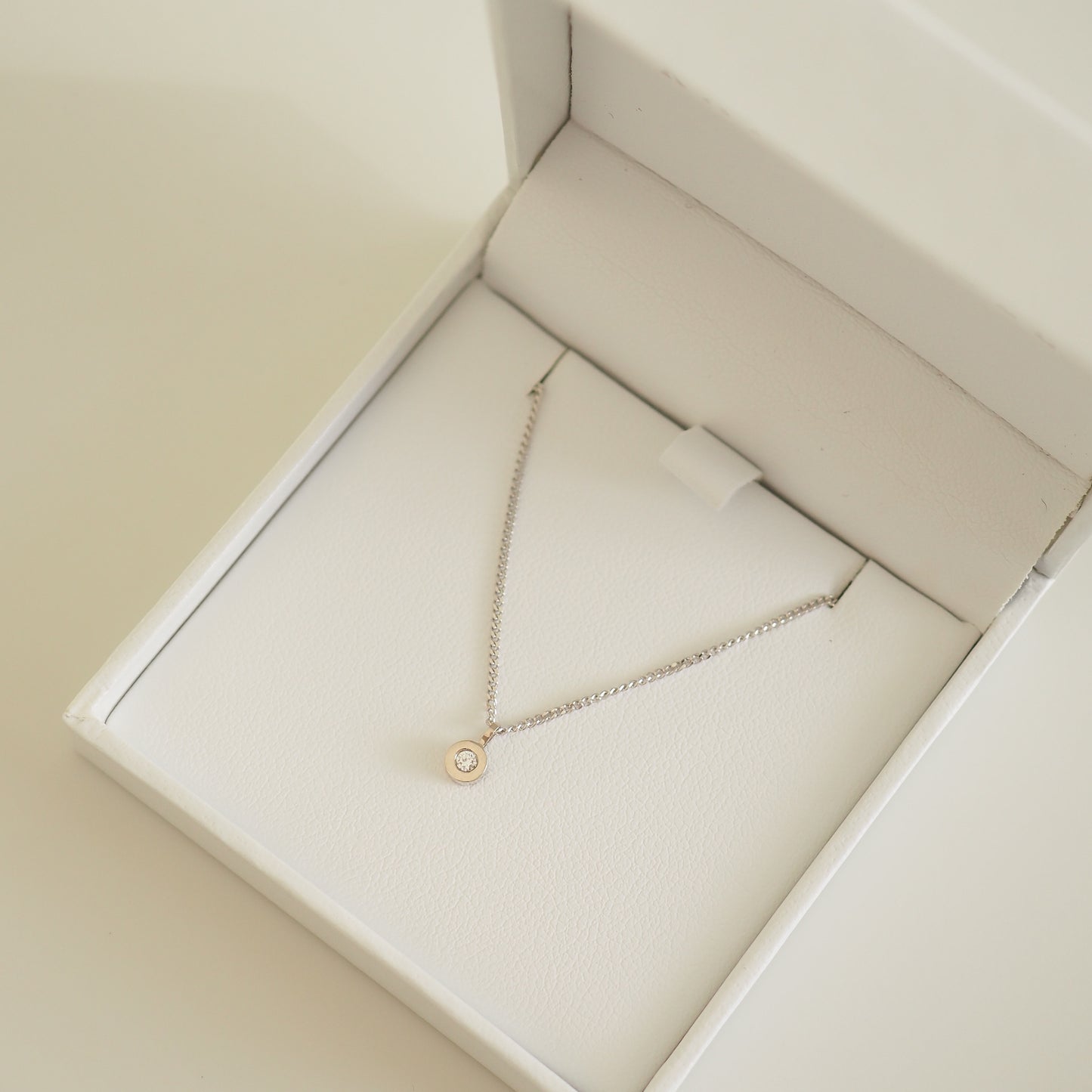 Elegant necklace with a small diamond pendant in a luxurious white presentation box, showcasing high-end jewellery design.