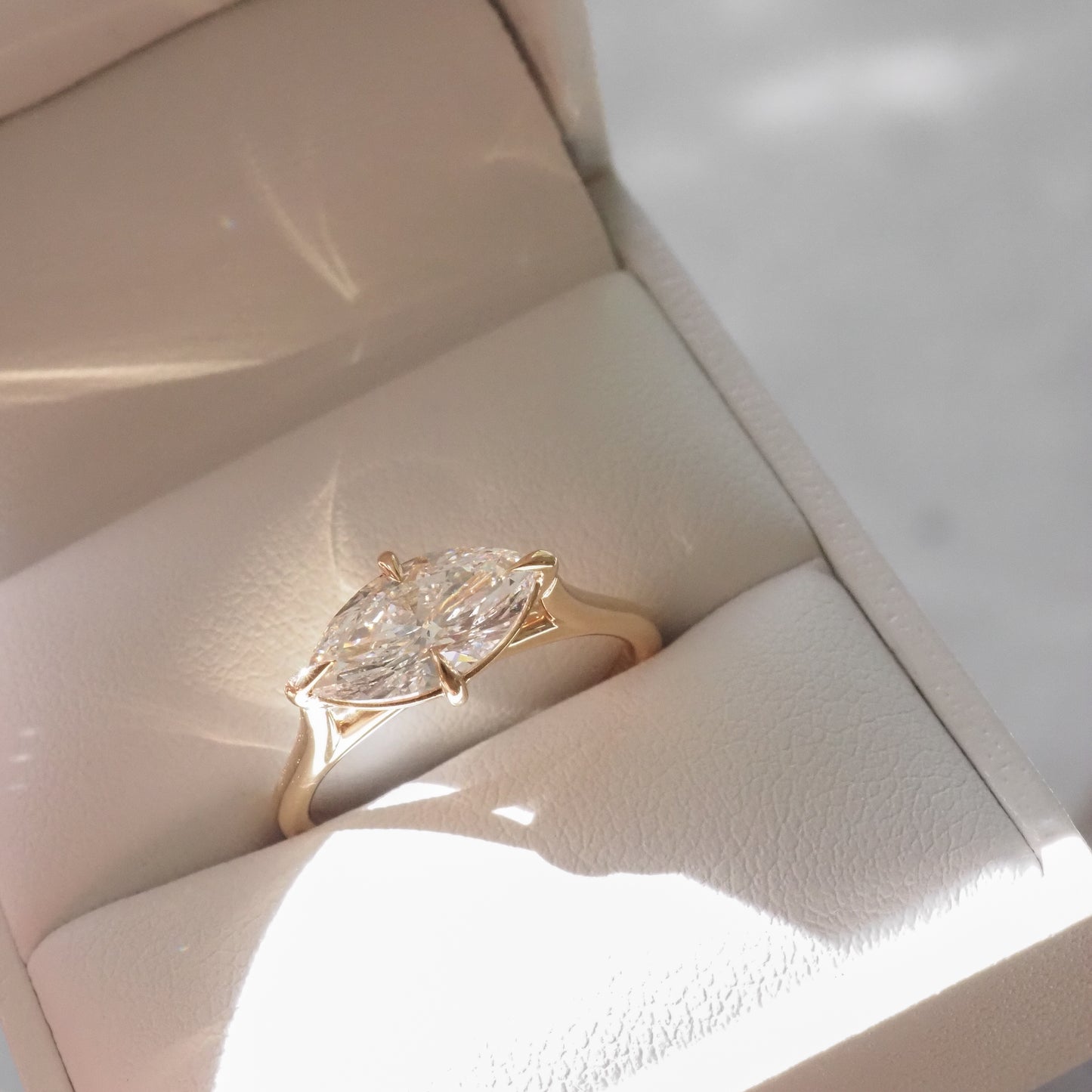 Marquise diamond ring in a gold setting, displayed in a cream jewellery box, reflecting light elegantly. Ideal for luxury jewellery enthusiasts.