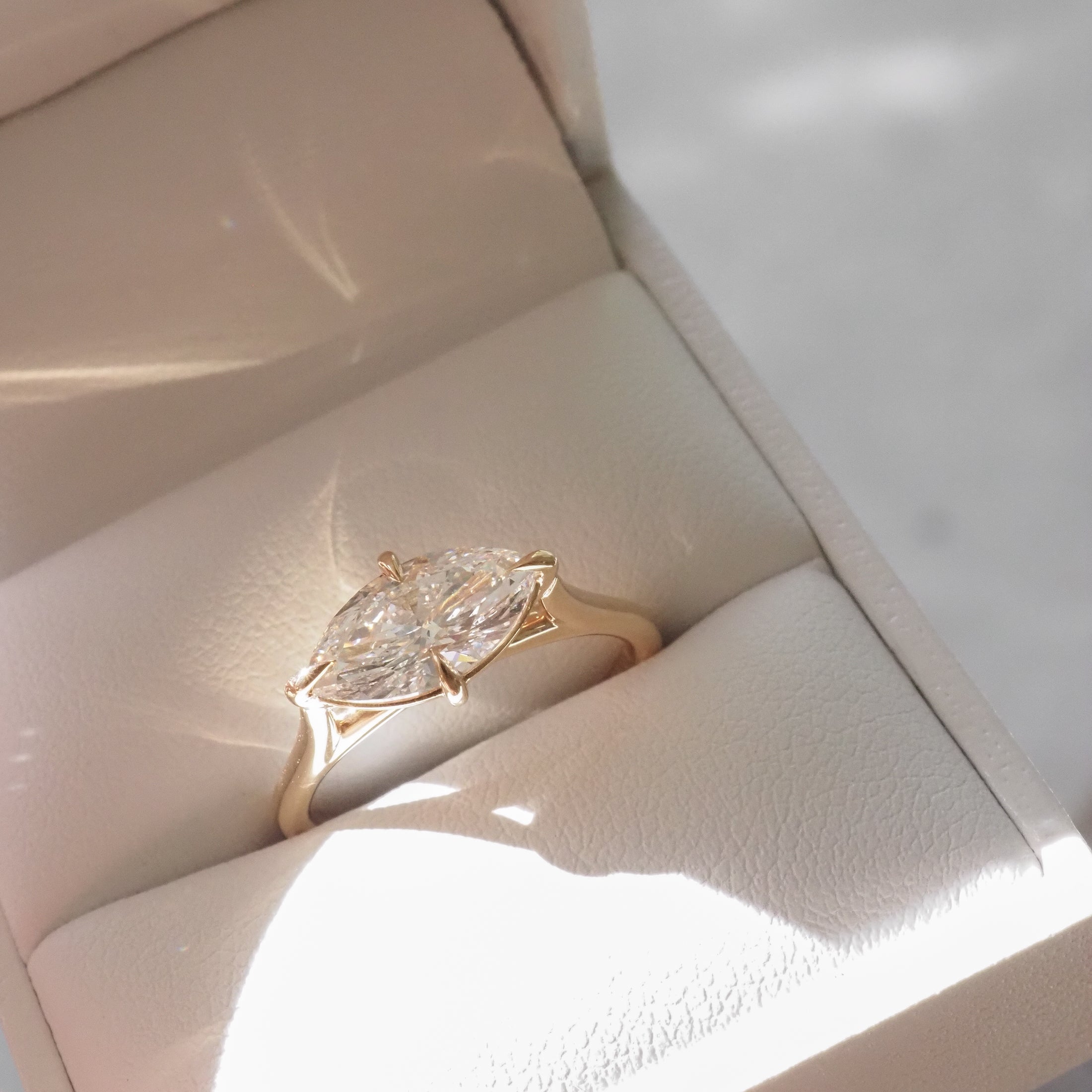 Marquise diamond ring in a gold setting, displayed in a cream jewellery box, reflecting light elegantly. Ideal for luxury jewellery enthusiasts.