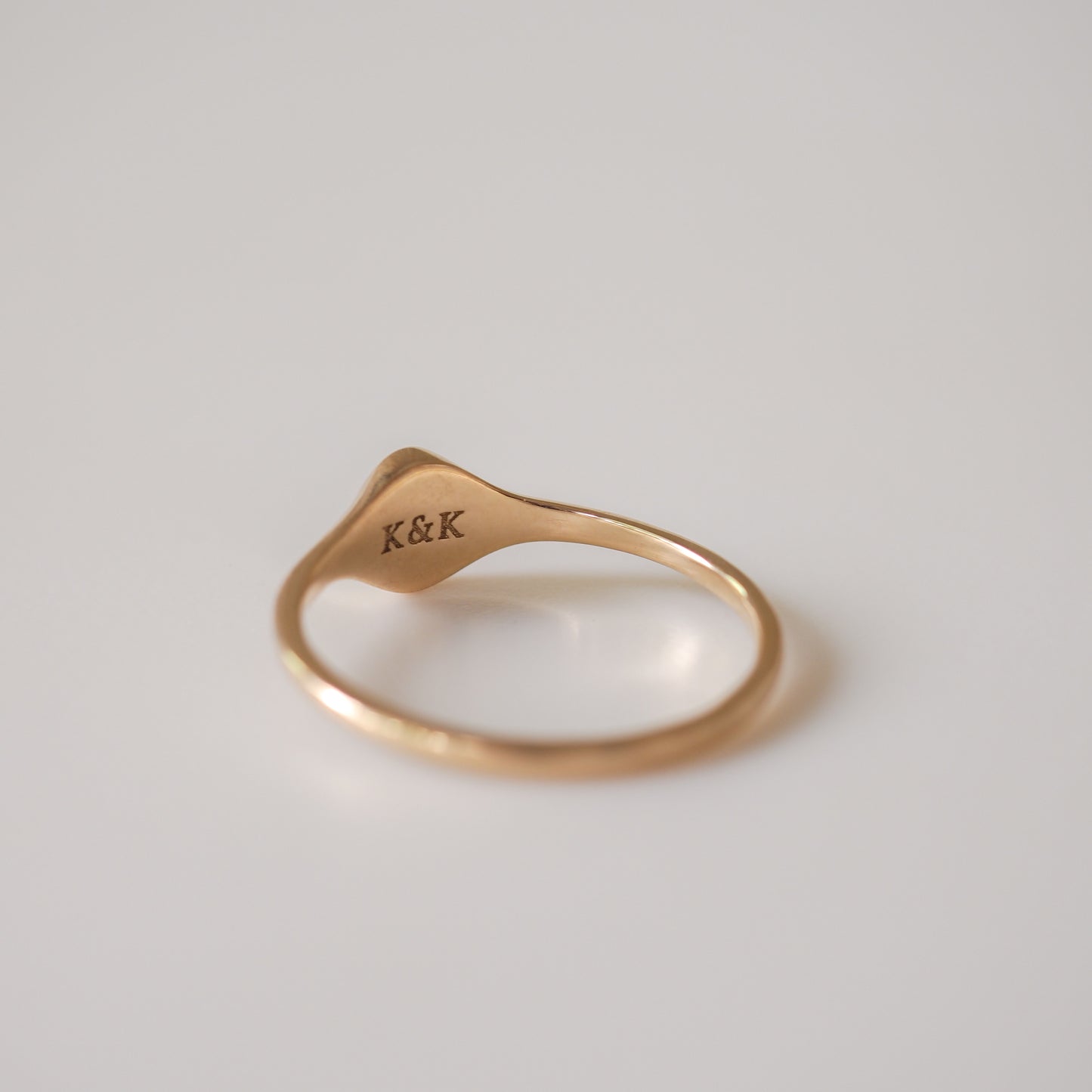 Elegant gold ring inscribed with "K&K" on a smooth, curved band against a soft white background. Luxury jewellery focus.
