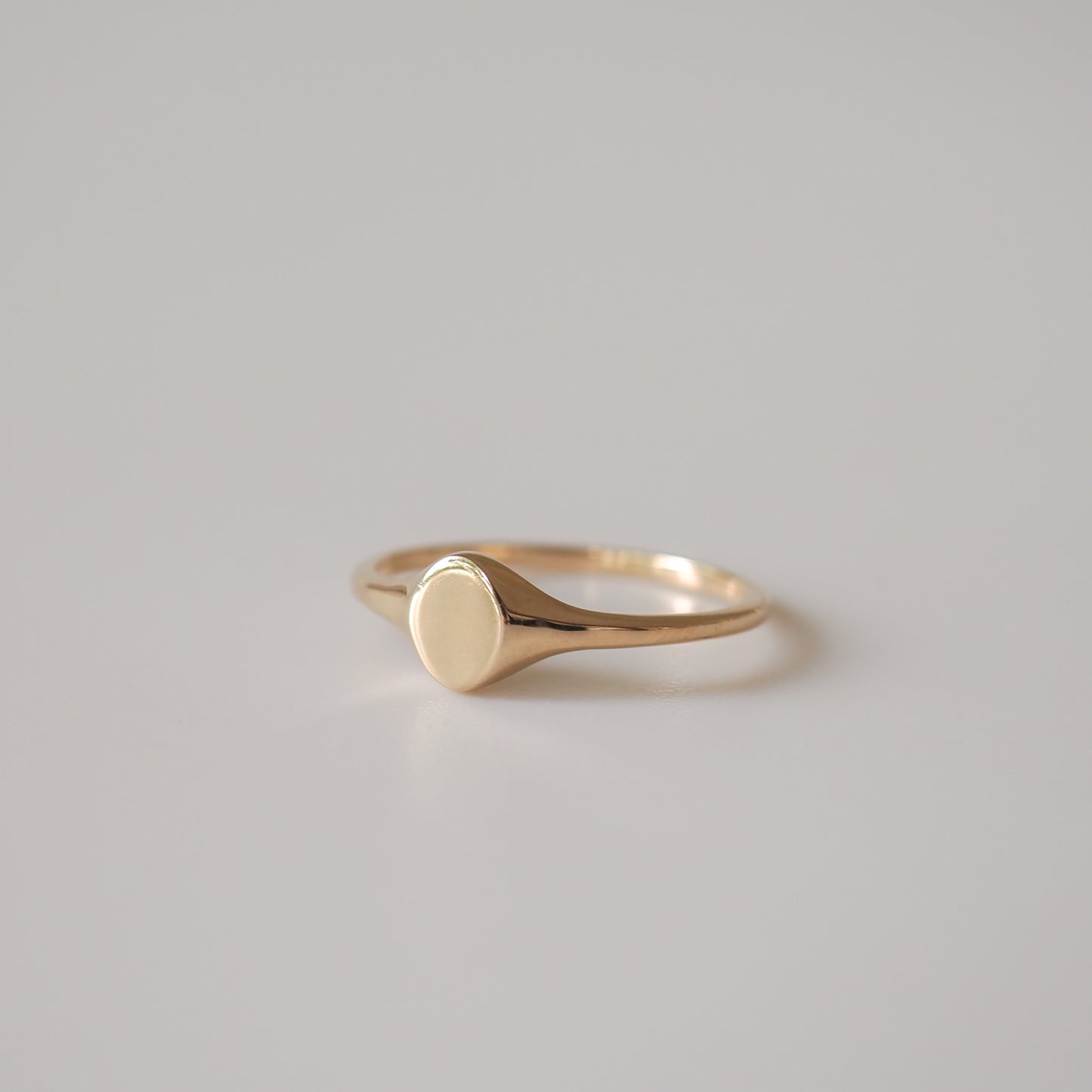 Elegant gold signet ring with a smooth, polished surface, set against a neutral grey background. Perfect for luxury jewellery collections.