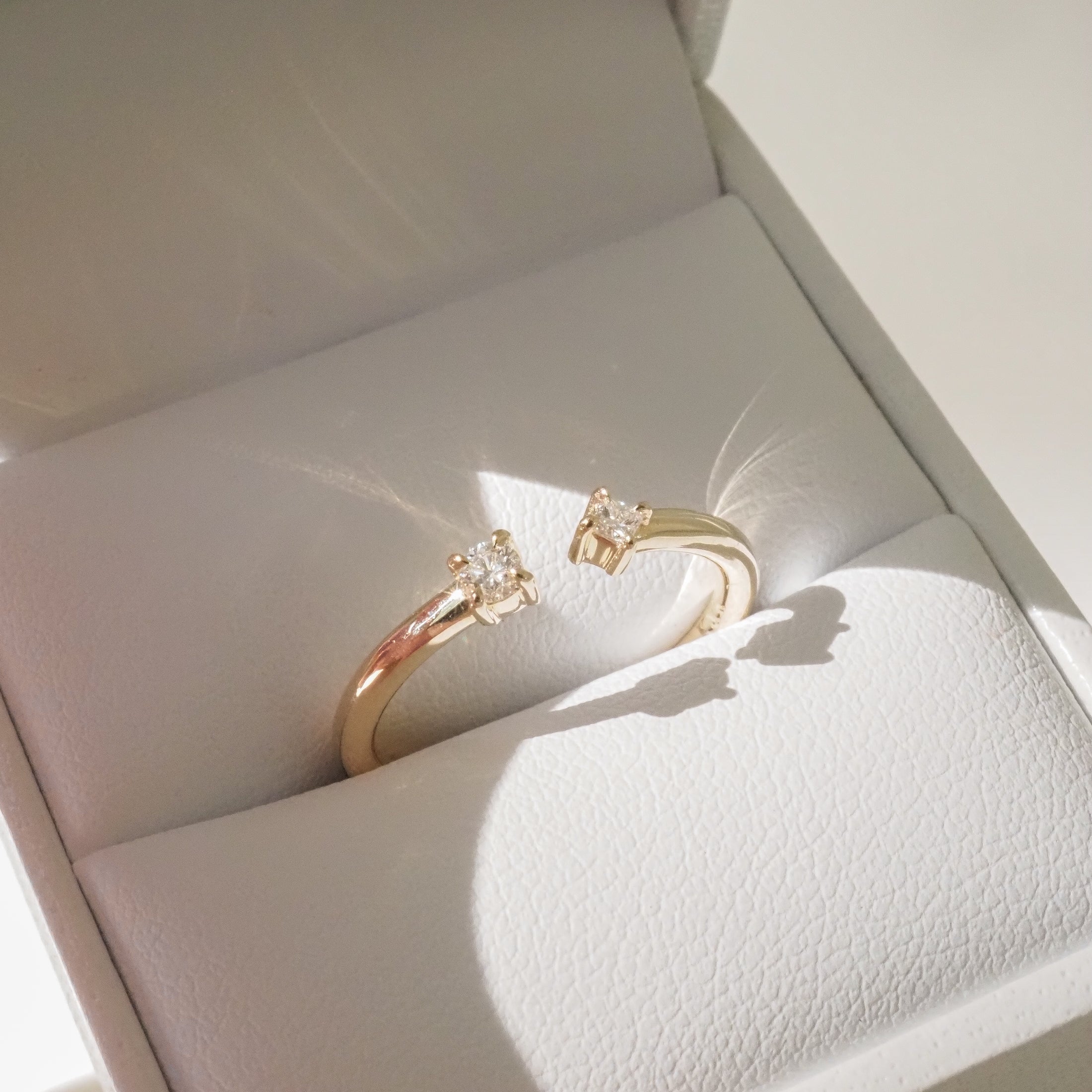 Gold rings with diamond solitaires in a white jewellery box, reflecting light. Perfect for luxury engagement or wedding accessories.