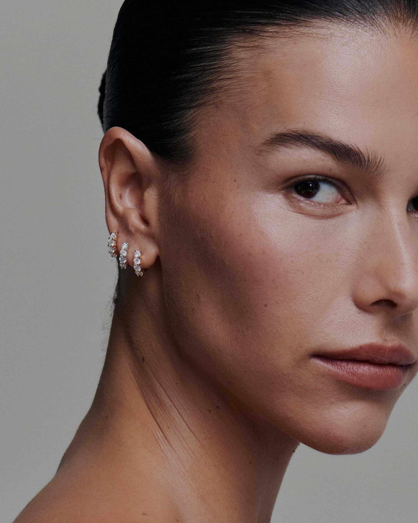 Close-up of a woman wearing diamond earrings against a neutral background