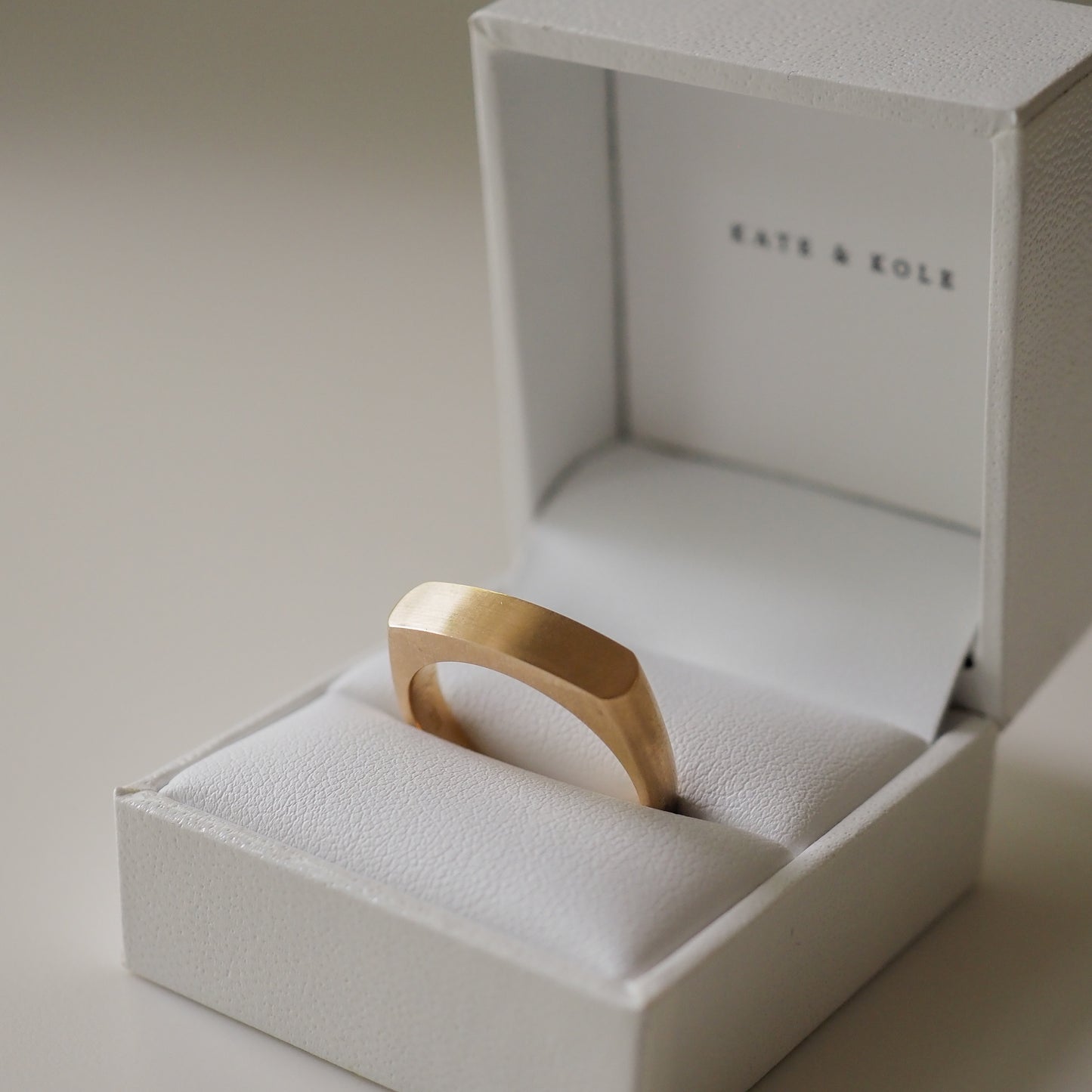 Minimalist gold ring with a flat top in a white Kate & Kole jewellery box, showcasing luxury design and craftsmanship.