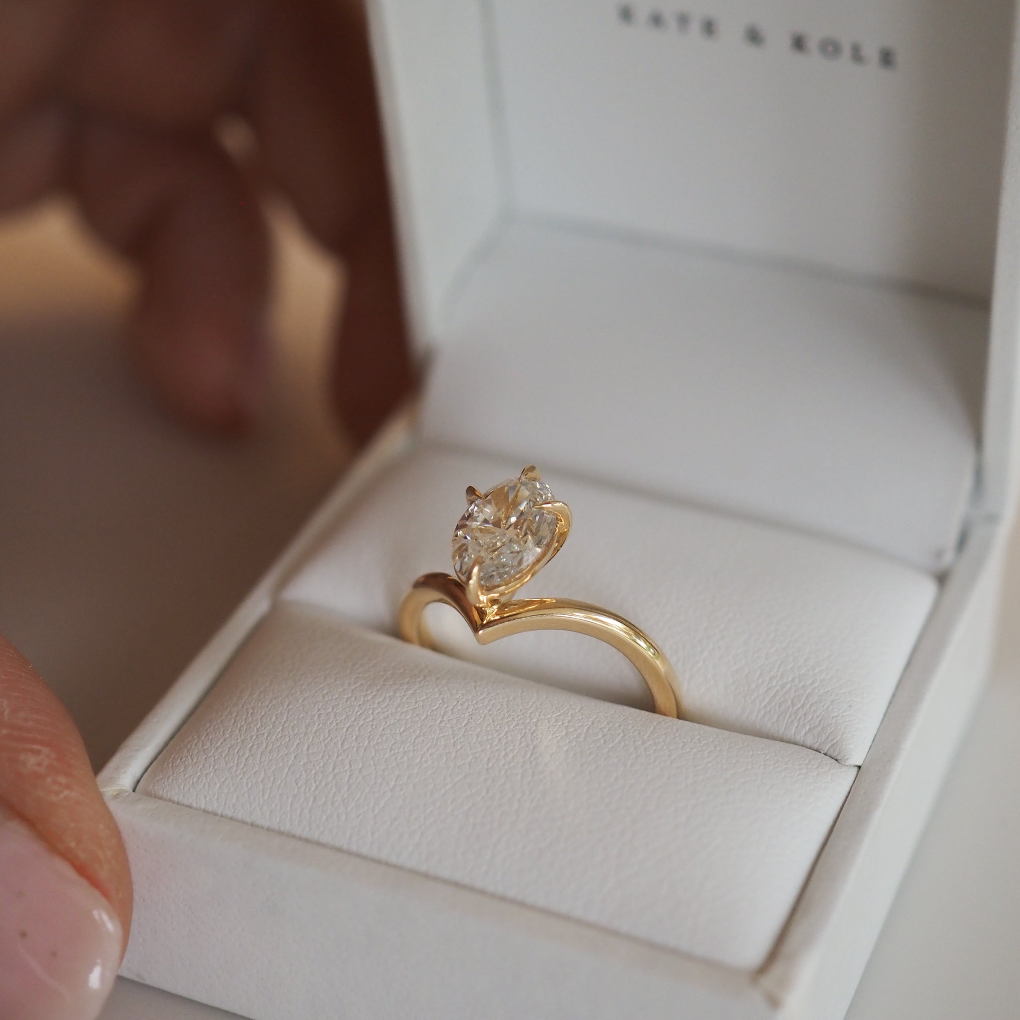 Gold engagement ring with a large pear-shaped diamond in an open box. Luxurious jewellery showcased in an elegant white case.