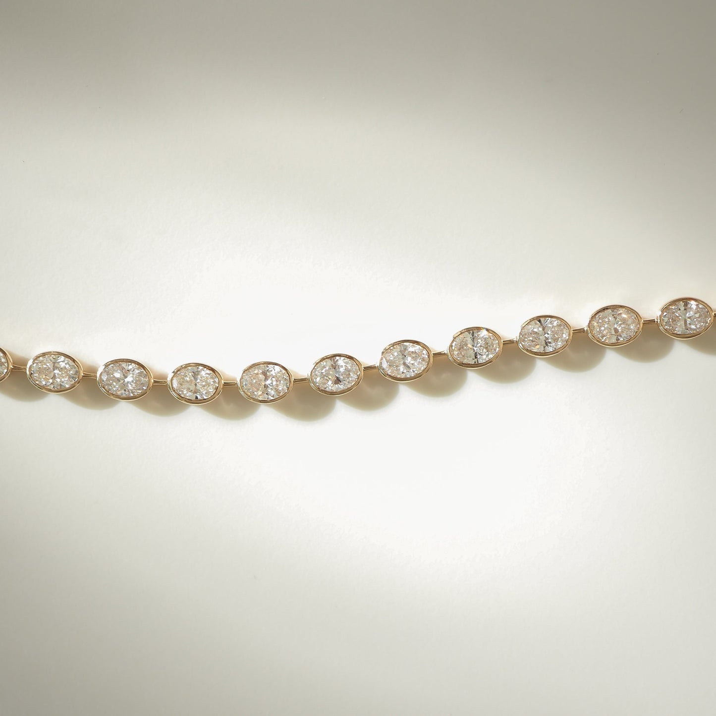 Elegant diamond bracelet with small, round diamonds set in gold links, displayed on a soft, pale background. Luxury jewellery piece.