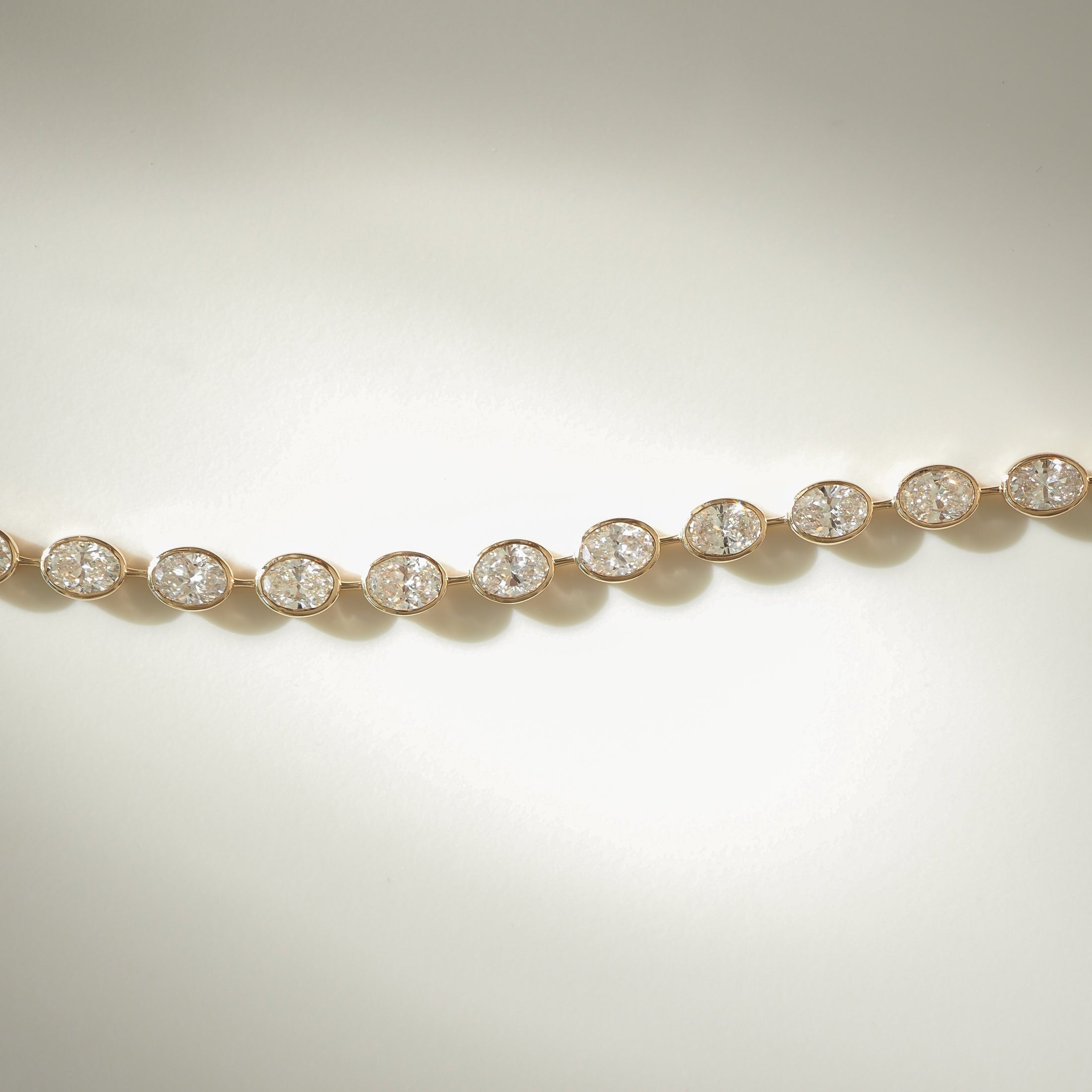 Elegant diamond bracelet with small, round diamonds set in gold links, displayed on a soft, pale background. Luxury jewellery piece.
