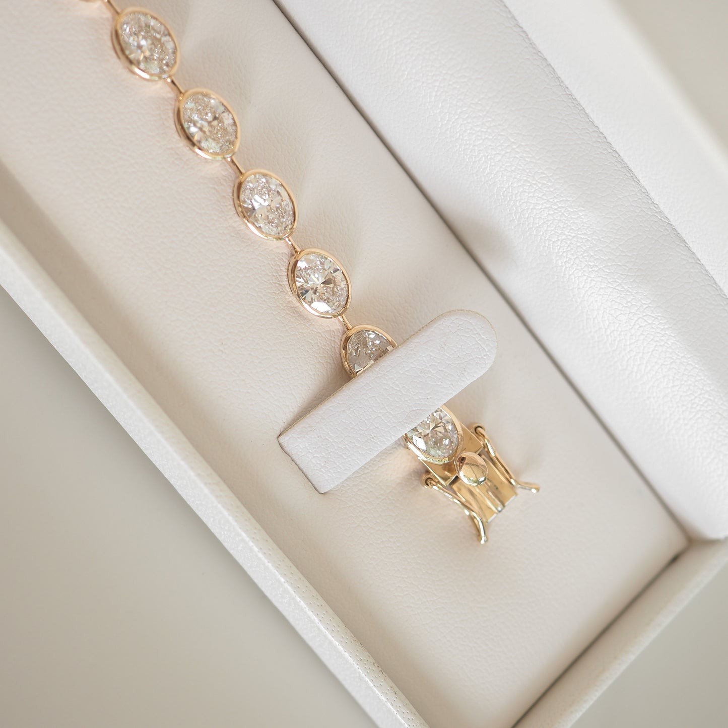 Gold bracelet with oval diamond clusters in a white jewellery box, showcasing luxury design and elegance.