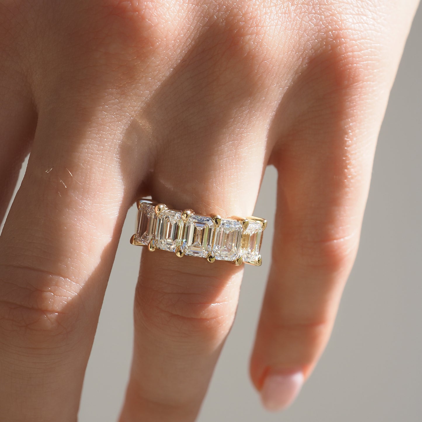 Hand wearing a luxury gold ring with rectangular diamonds, showcasing elegance and high-end jewellery in natural light.