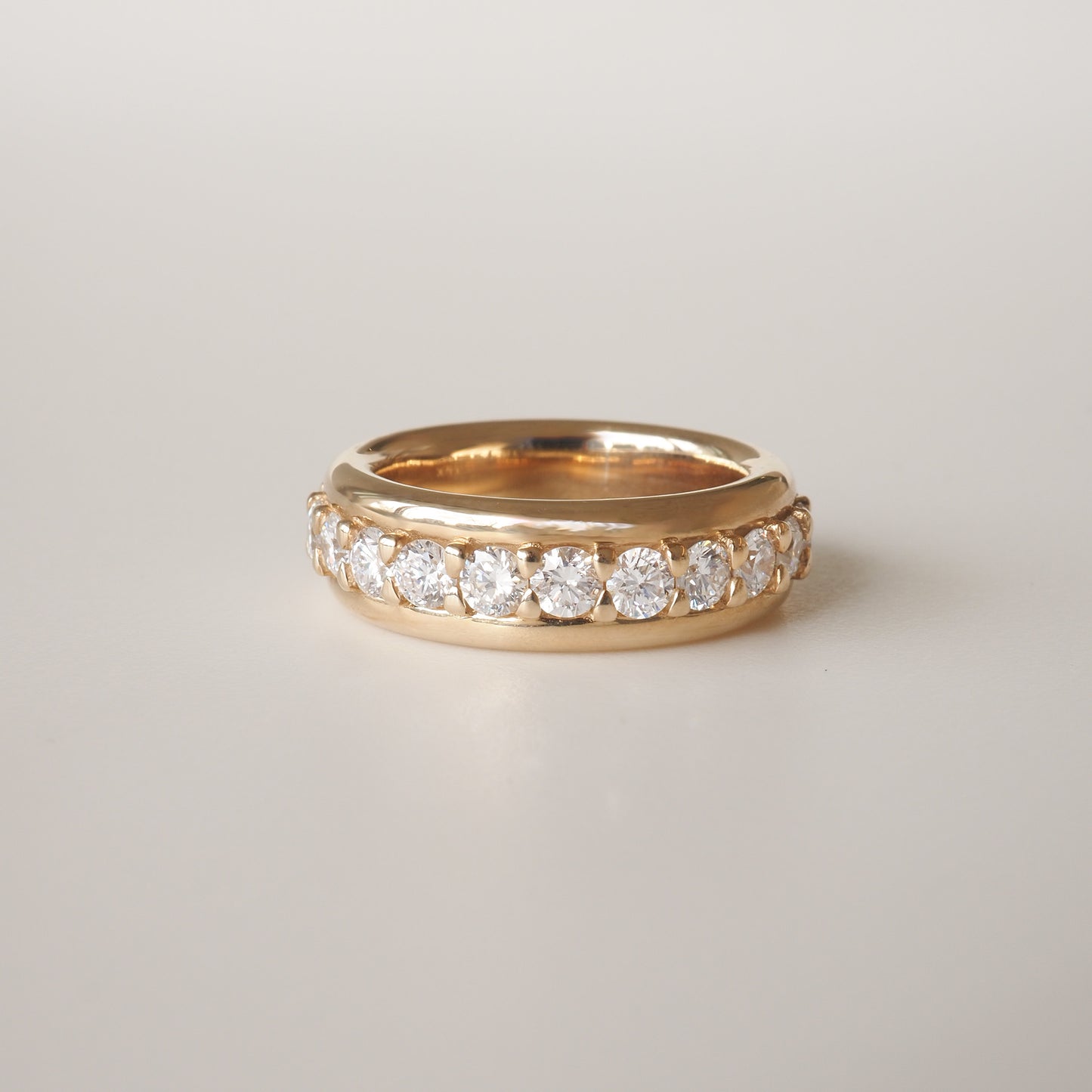 Gold ring with a row of sparkling diamonds set around the band, displayed on a plain background. Luxurious jewellery design.