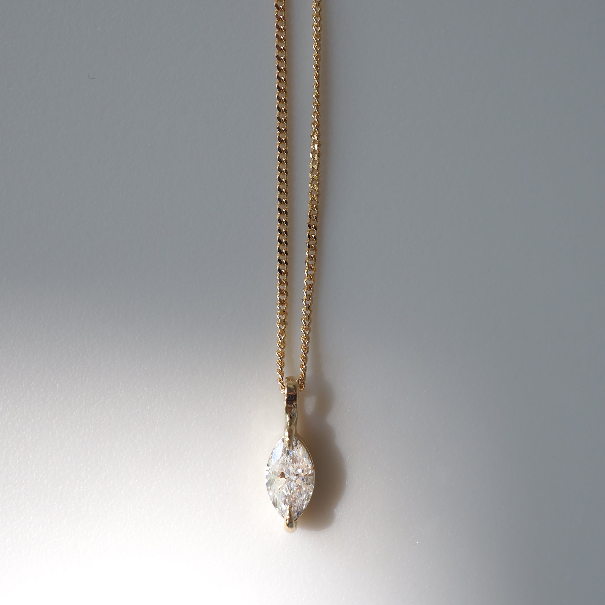 Gold chain necklace with marquise-cut diamond pendant, elegantly displayed against a neutral background, showcasing luxury jewellery design.