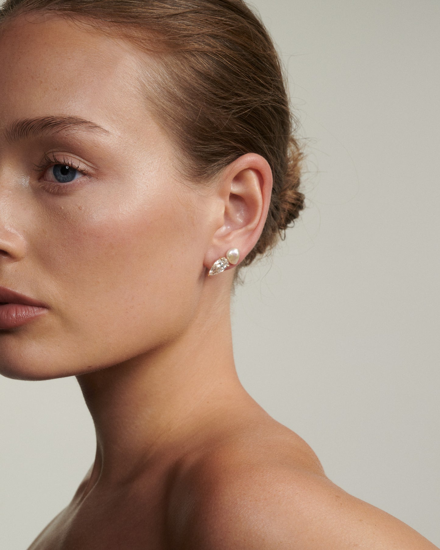 Close-up of a woman wearing diamond and pearl earrings against a neutral background