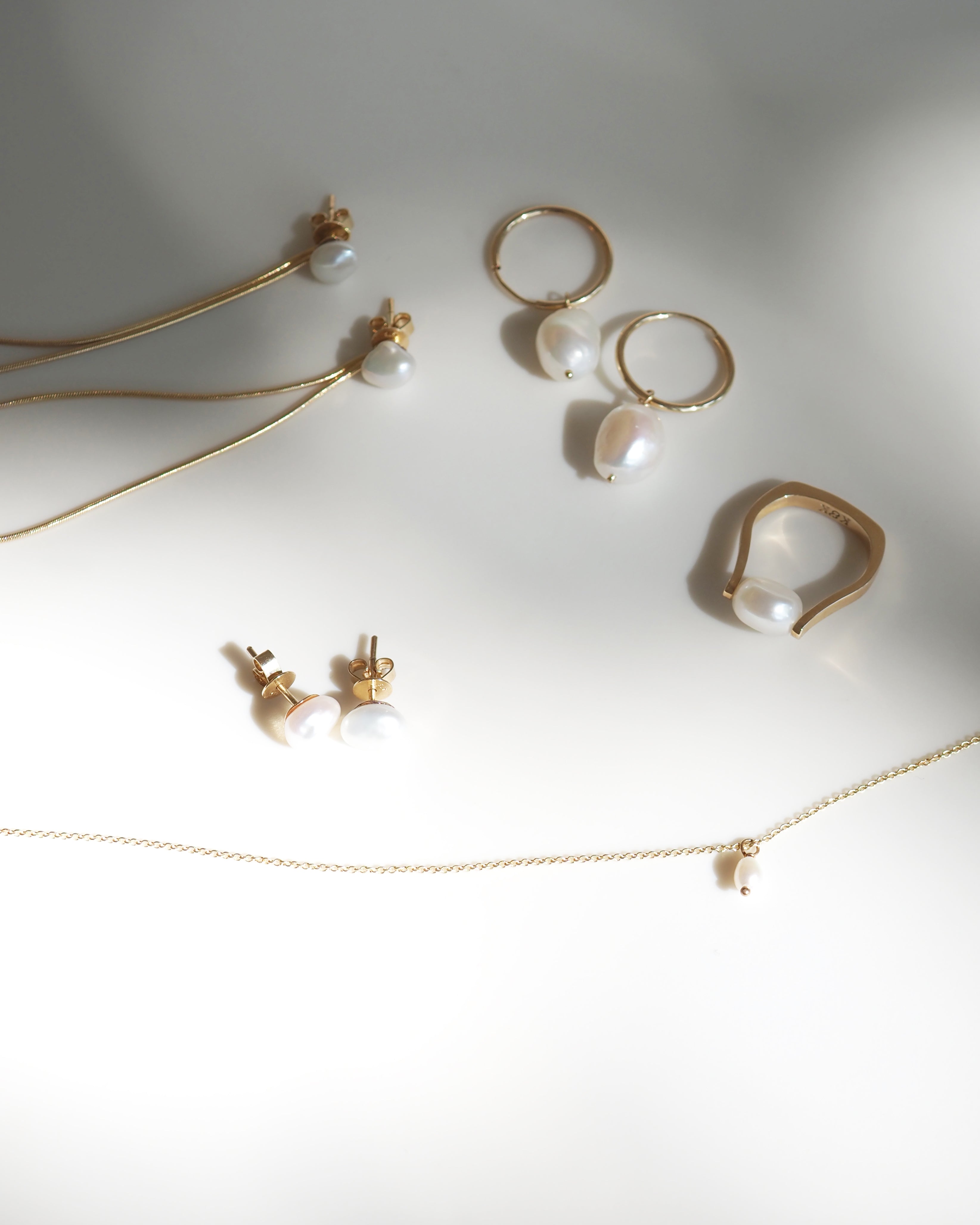 Elegant gold jewellery set with pearls, featuring earrings, a ring, and a necklace, beautifully arranged on a soft white background.