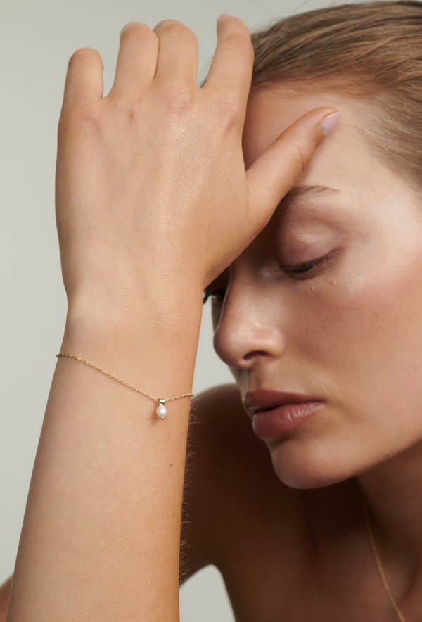Woman wearing a gold bracelet with a pearl on a neutral background