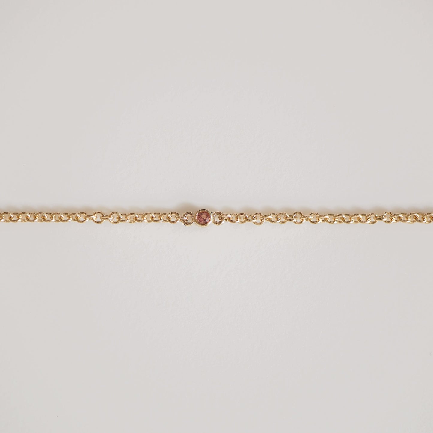 Gold chain with a single, small pink diamond in the centre. Elegant and minimalist luxury jewellery on a plain white background.