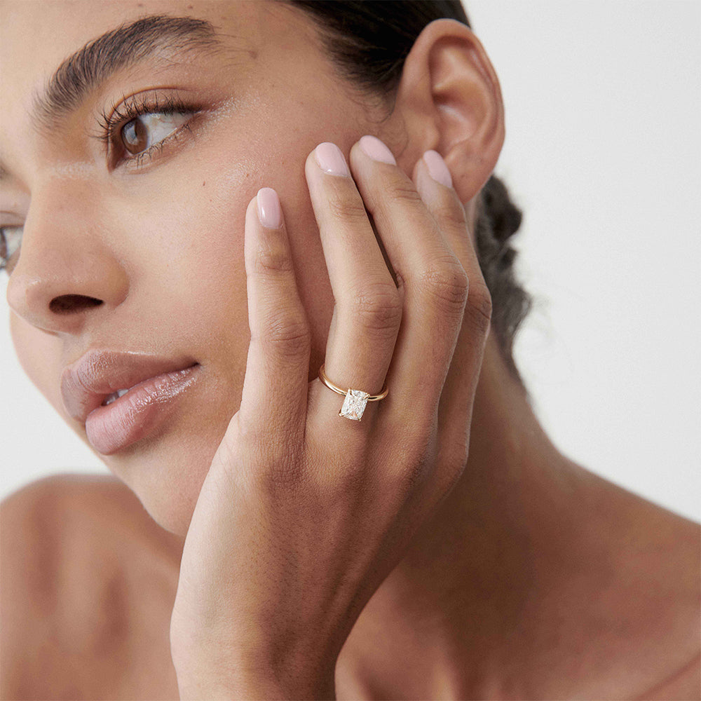 Close-up of a woman showcasing a solitaire diamond ring on her finger, with a soft, neutral background.[text overlay: 1.5ct Diamond]
