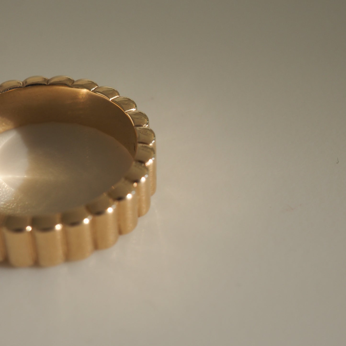 Gold scalloped edge ring on a neutral background, showcasing luxury jewellery design with a textured finish.