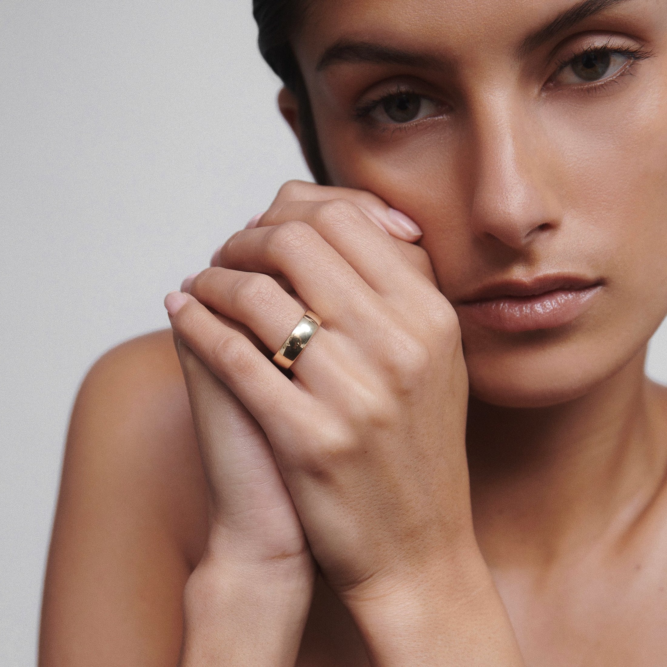 Woman wearing a polished gold ring on her finger, thoughtfully posed against a neutral background. Elegant and minimalist luxury jewellery.