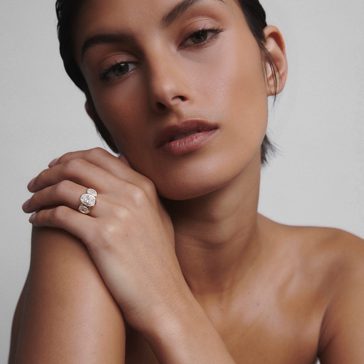 Woman wearing a luxurious diamond and gold ring against a neutral background, highlighting elegant jewellery design.