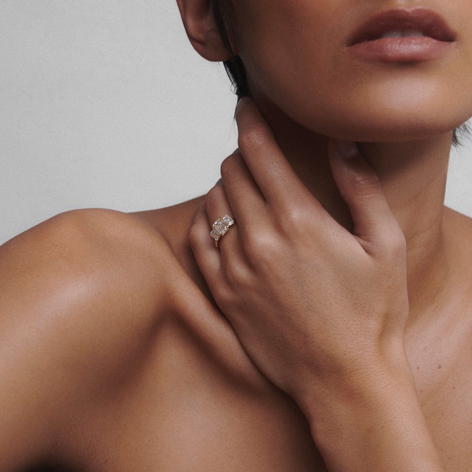 Woman showcasing a luxury diamond ring on her hand, soft lighting accentuates her shoulder and neck, highlighting the jewellery's elegance.