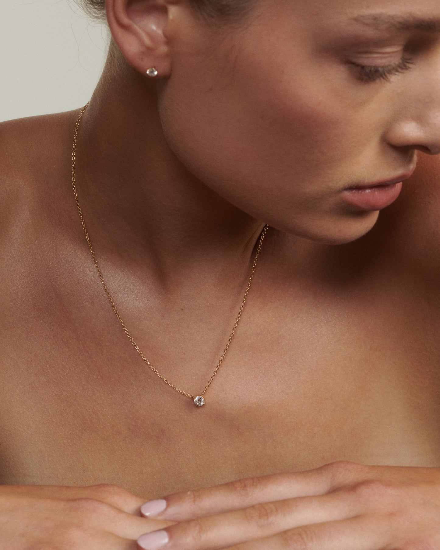 Close-up of a woman wearing a gold necklace with a small pendant. [text overlay: Andrea wears the 0.5ct Round Diamond Necklace]