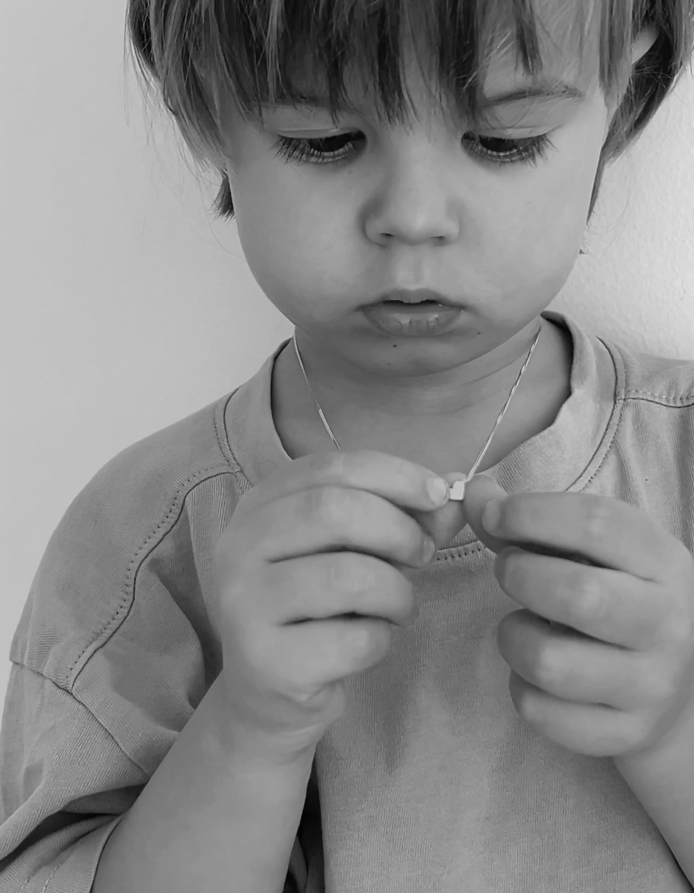 Young child examines a delicate necklace in black and white, showcasing fine jewellery. Toddler's focus highlights intricate design details.