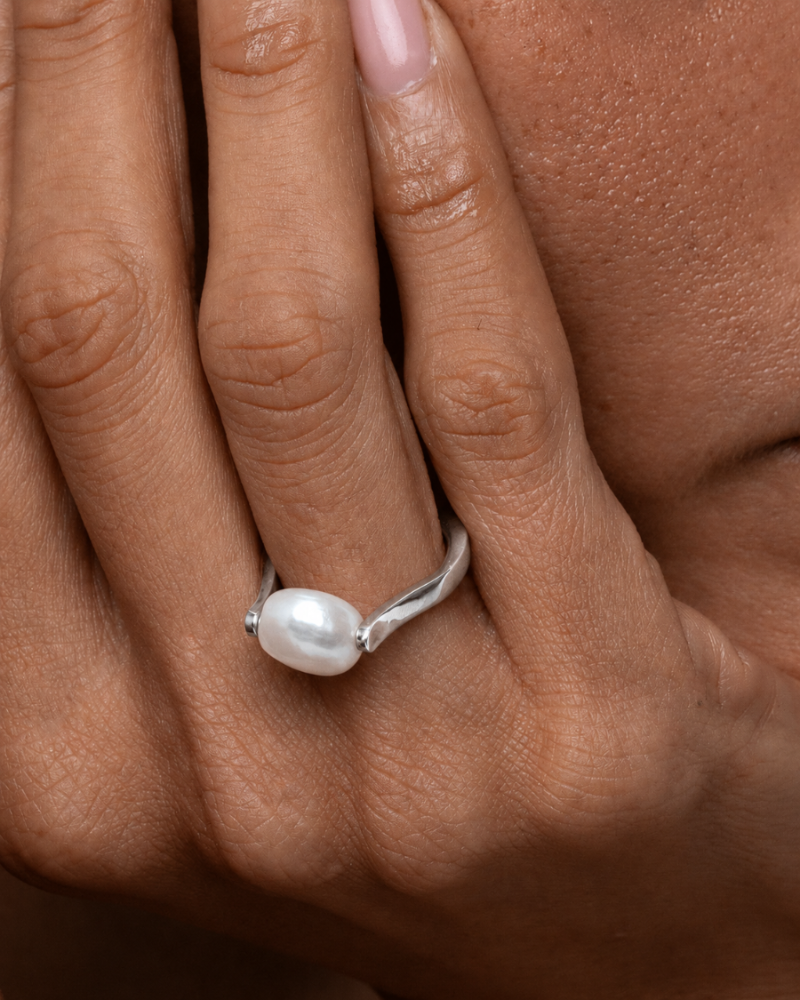 Close-up of a hand wearing a silver ring with a pearl on a neutral background