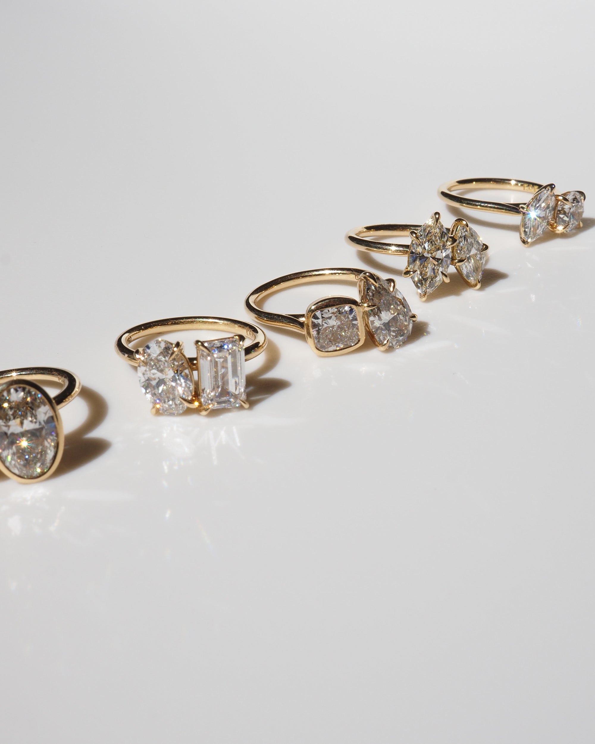 A row of five gold rings, each with unique diamond cuts, displayed elegantly on a reflective surface, embodying luxury jewellery design.