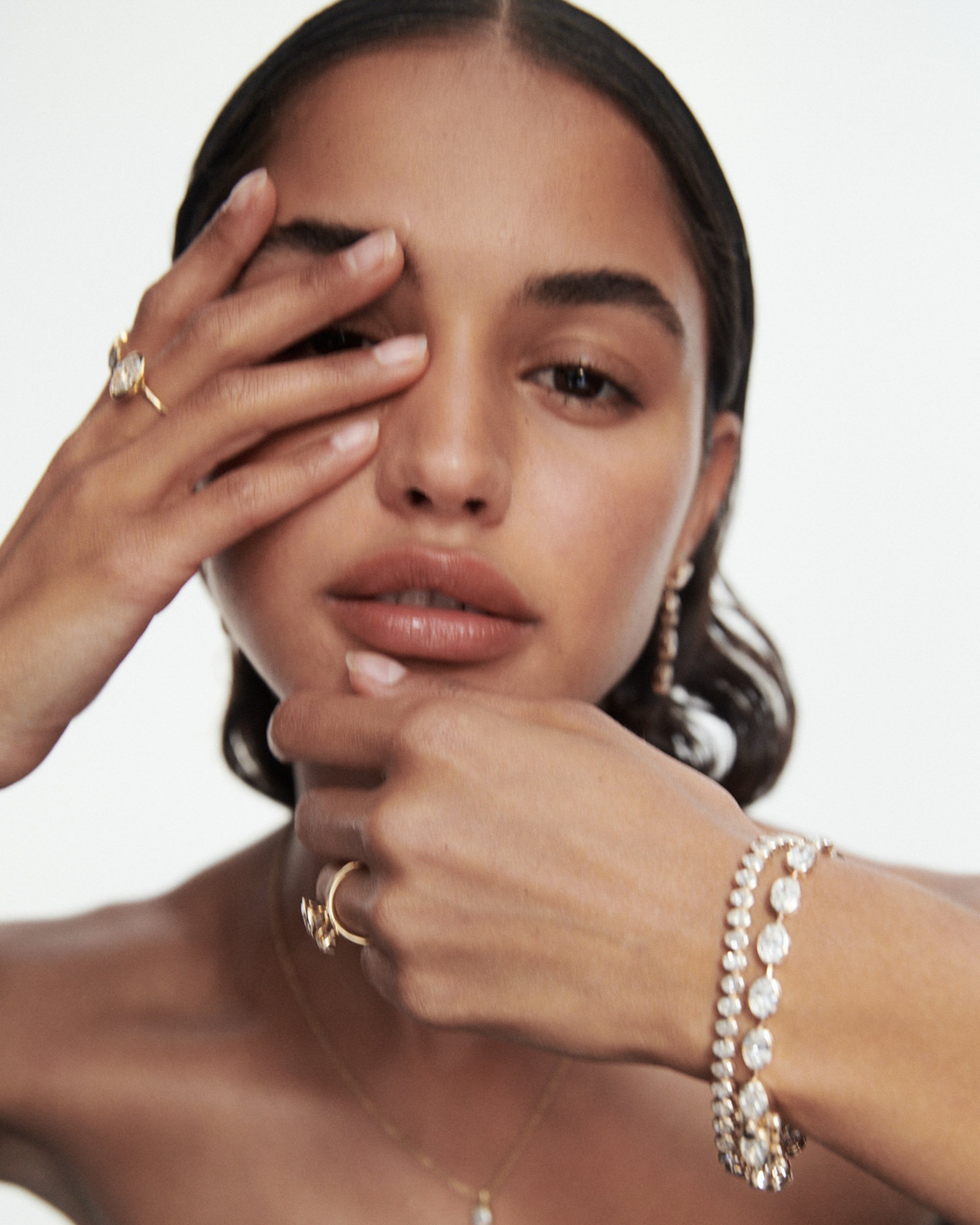 Woman adorned with elegant jewellery, featuring diamond bracelet, delicate rings, and earrings, striking a sophisticated pose against a soft background.