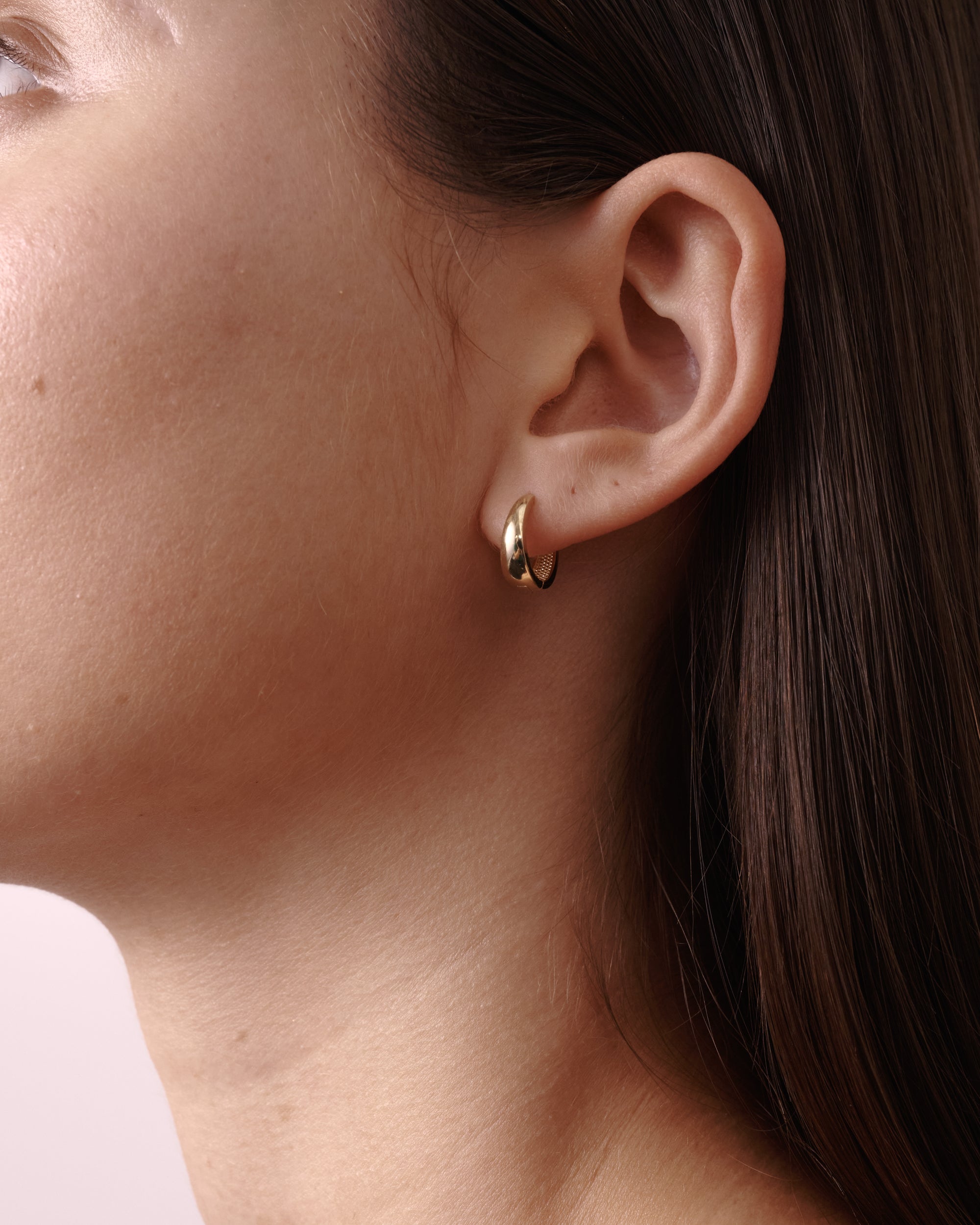 Close-up of a woman's ear wearing a sleek gold hoop earring. Emphasises minimalist luxury jewellery style.