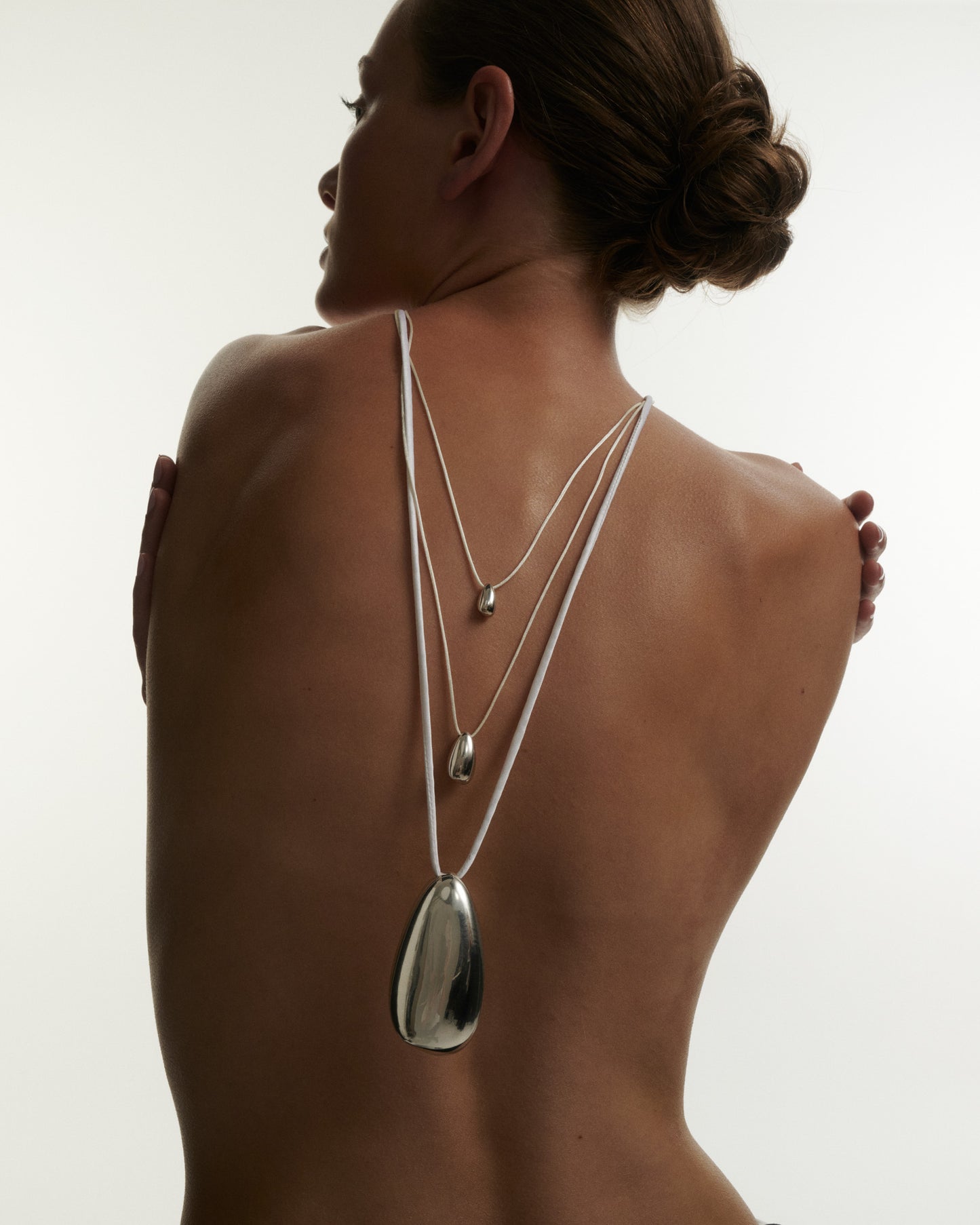 Woman wearing a silver necklace with a pendant on a plain background [text overlay: Andrea wears the Small and Large Toka Pendants & the Toka Perfume Pendant]