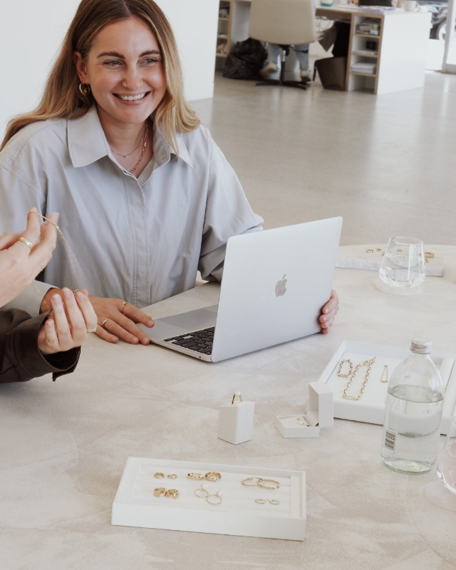Two people sitting at a table with a laptop, discussing something, in a modern office setting.