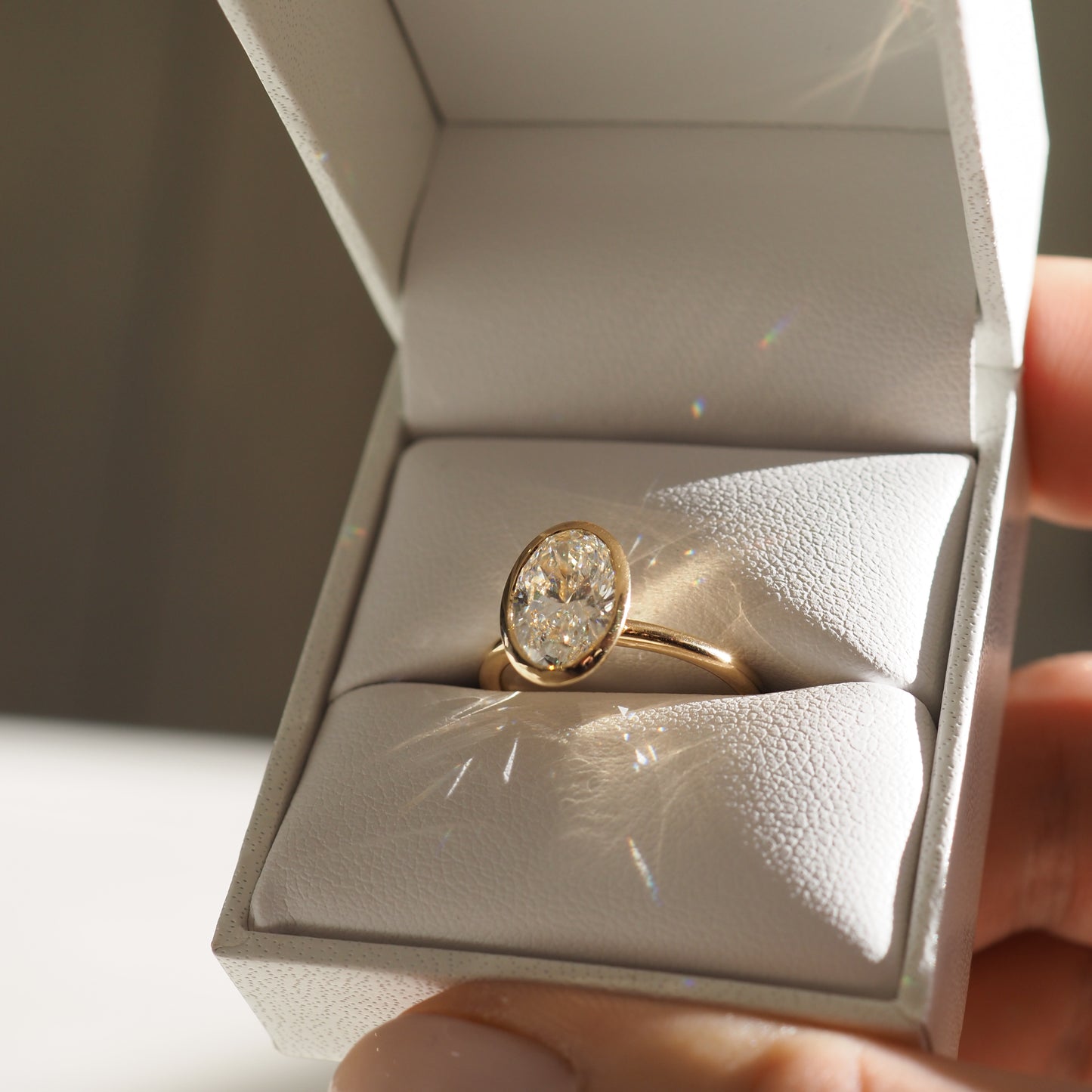 A gold band with an oval diamond ring displayed in an open white jewellery box, sparkling under soft light. Perfect for luxury engagements.