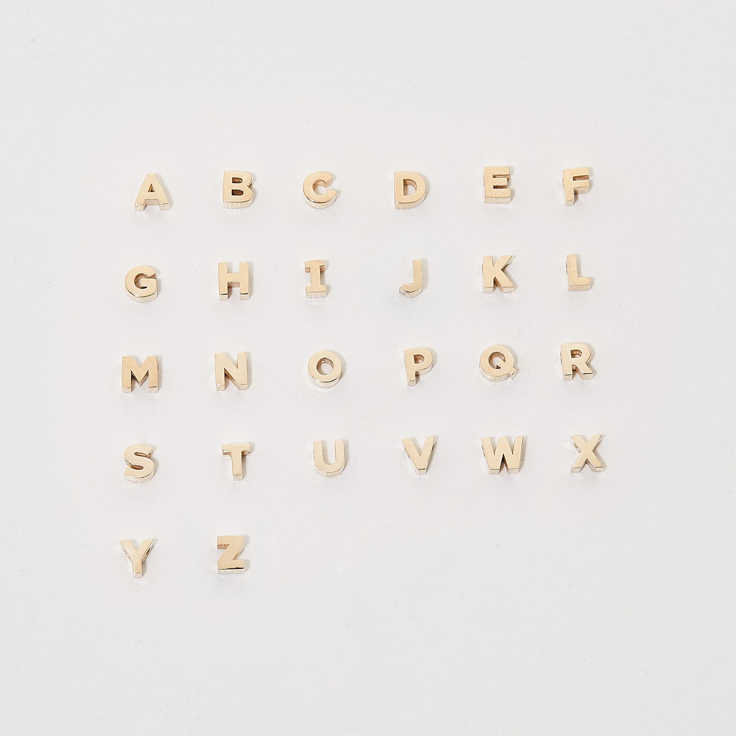 Gold alphabet pendant charms arranged alphabetically on a white background, showcasing luxury jewellery design.