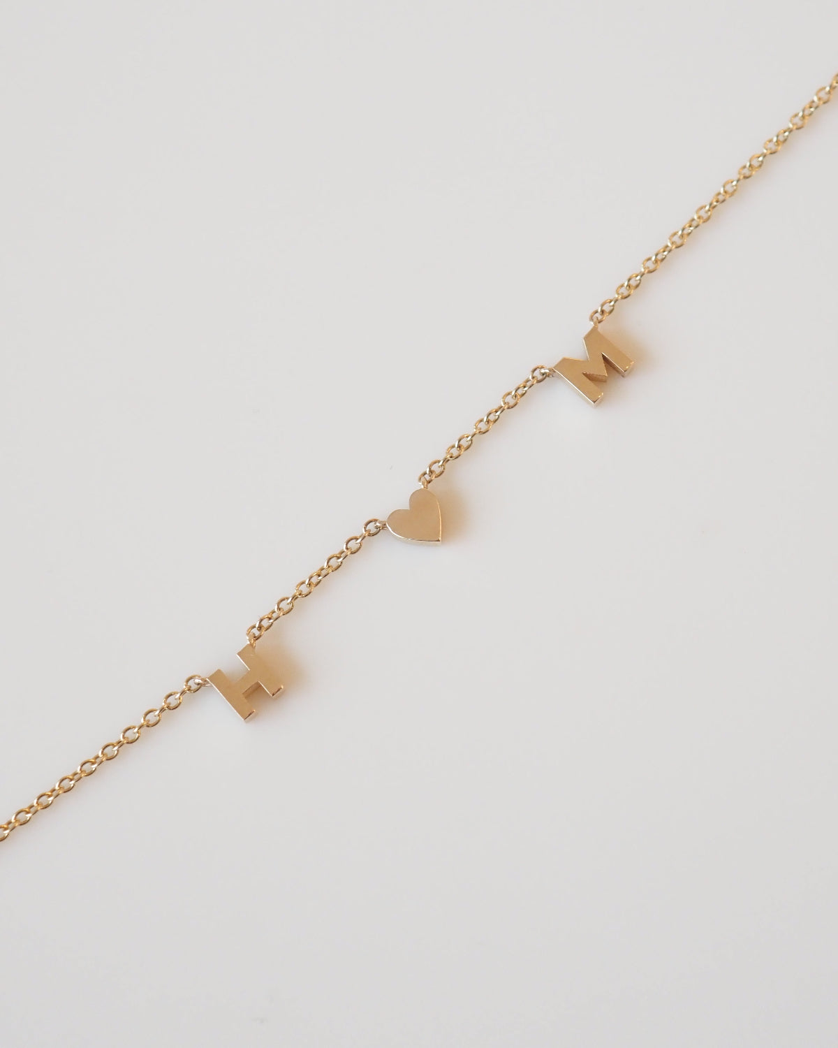 Gold necklace with heart and bow pendants on a light gray background [text overlay: Fixed Lovers]