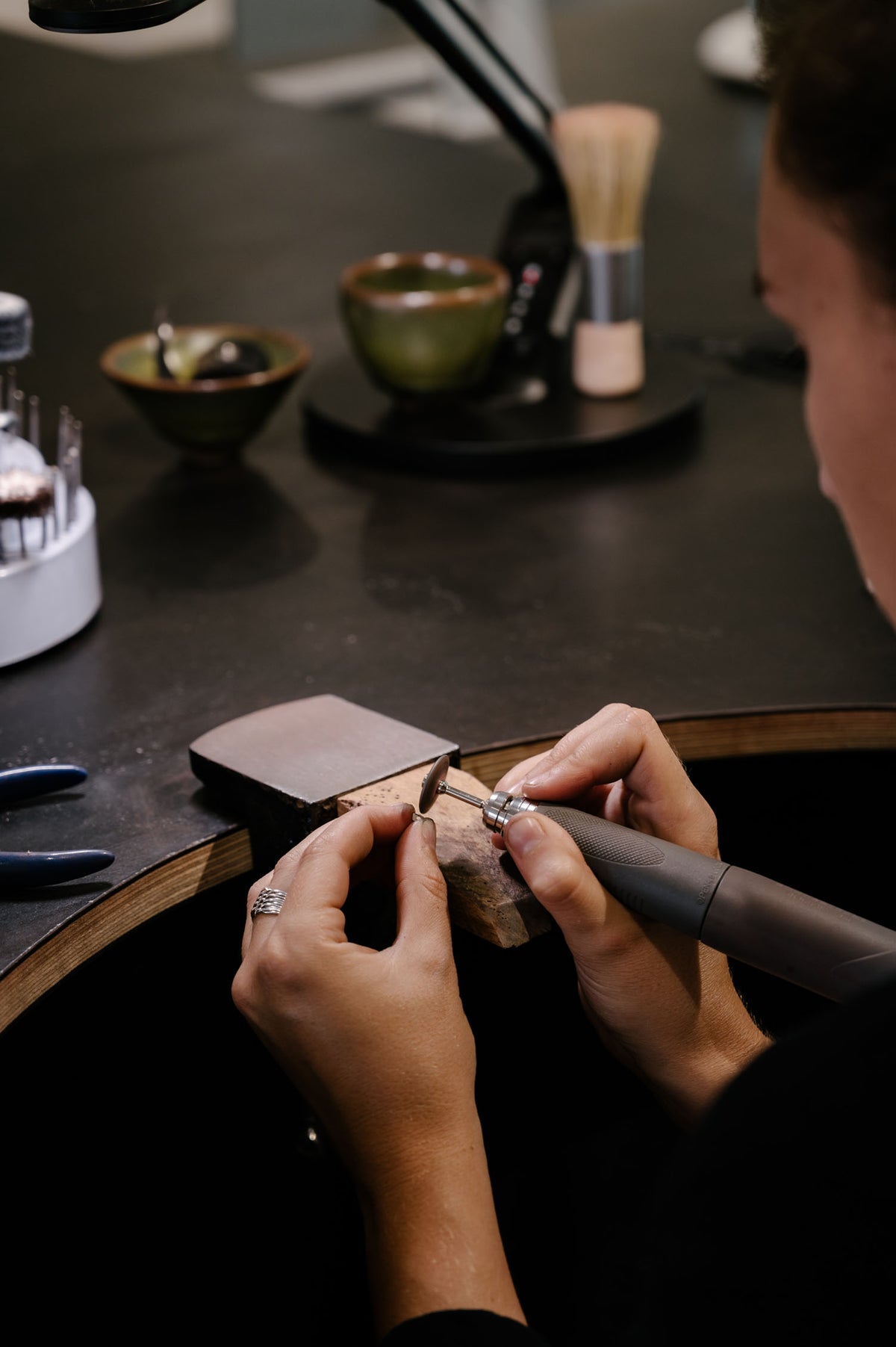 Hands crafting a luxury ring at a jewellery bench, surrounded by tools and materials, highlighting artisanal craftsmanship in fine jewellery.