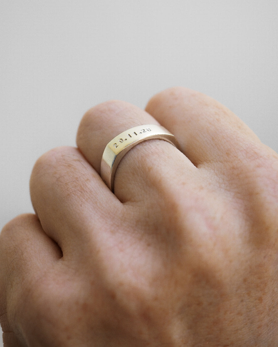Gold ring with engraved text on a person's finger against a neutral background