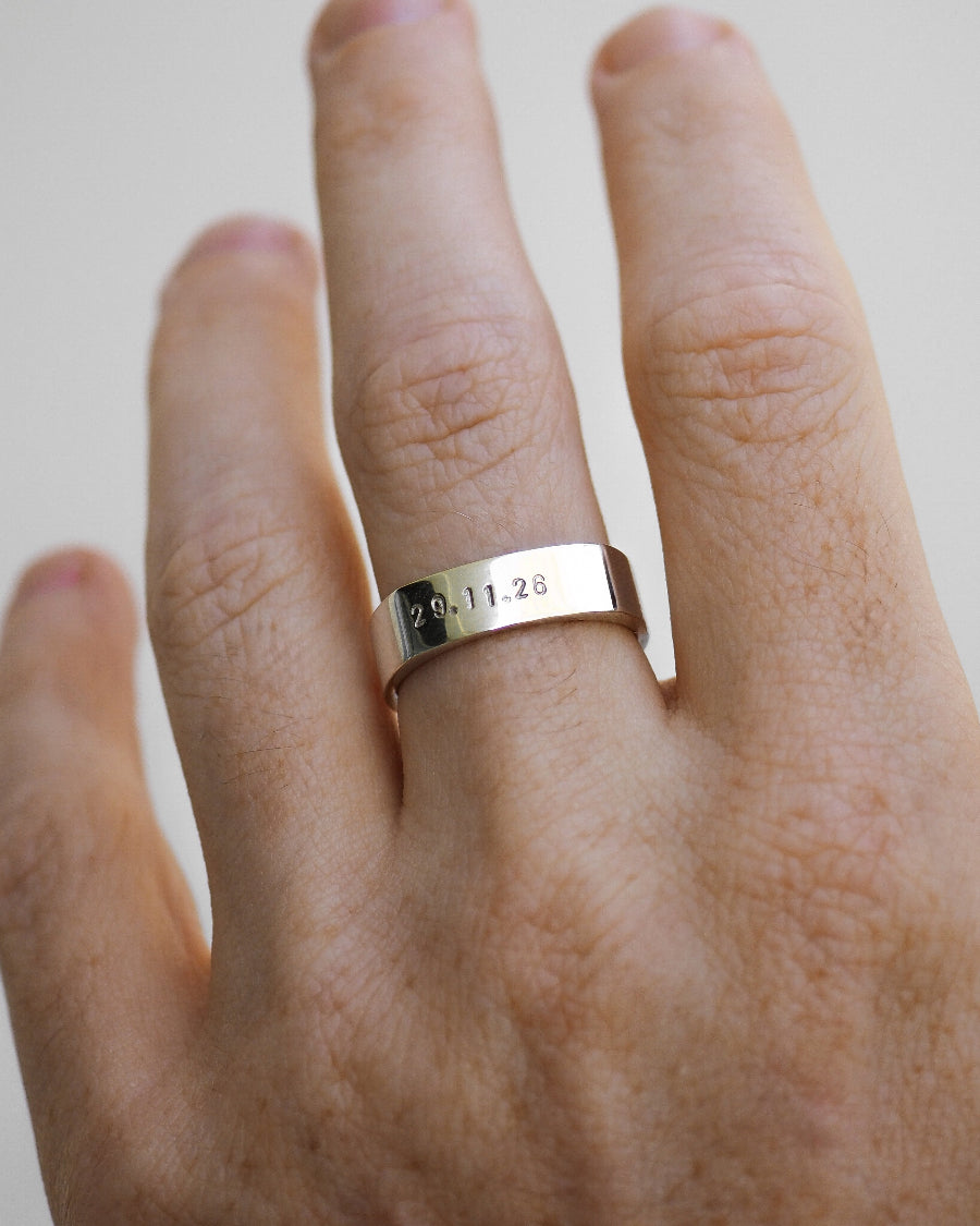 Silver ring with engraved date on a person's finger against a plain background